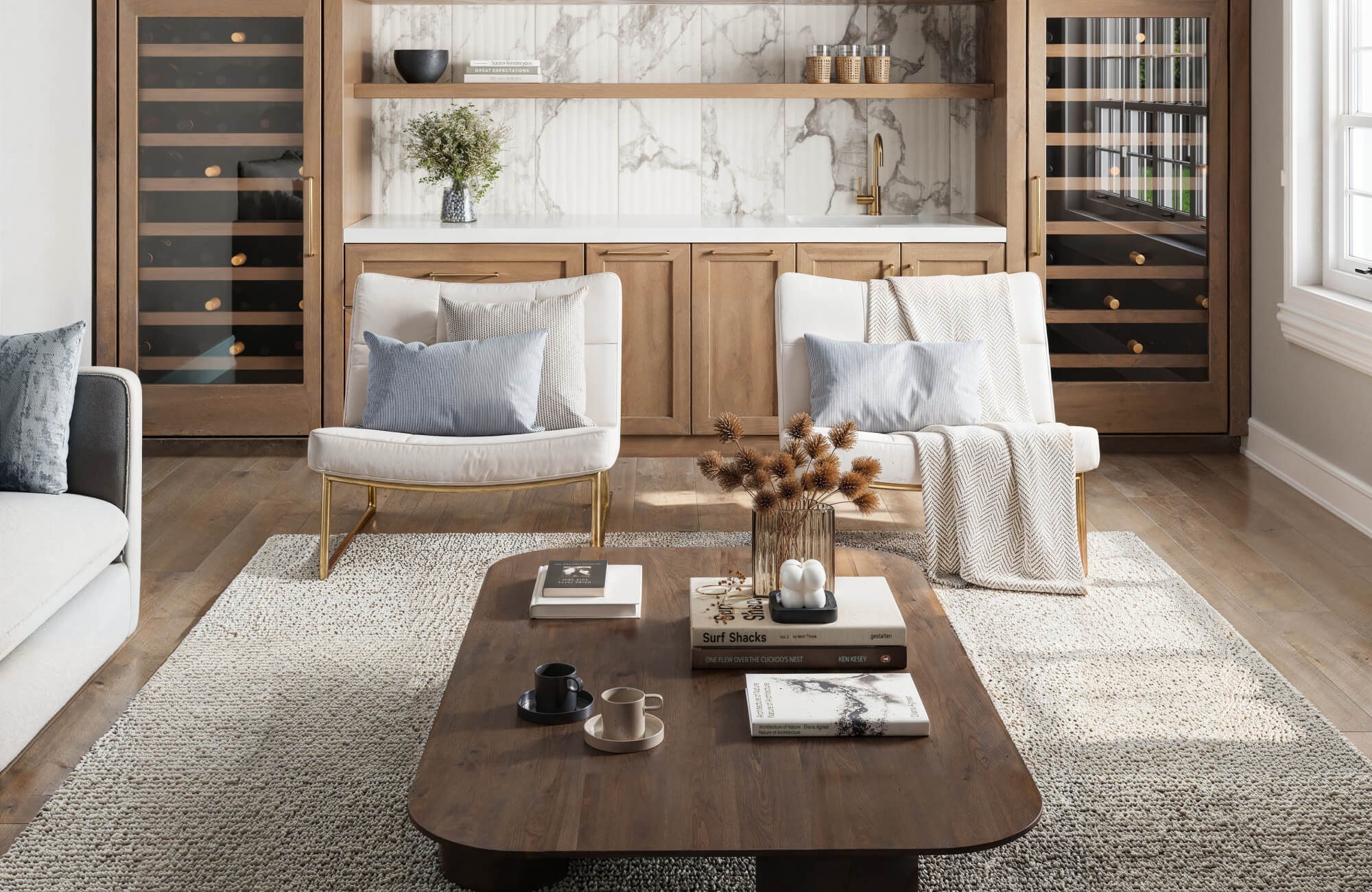 Elegant sitting area with cozy seating, a rich wood coffee table, and a plush textured 9x12 rug complementing a marble-accented wet bar.