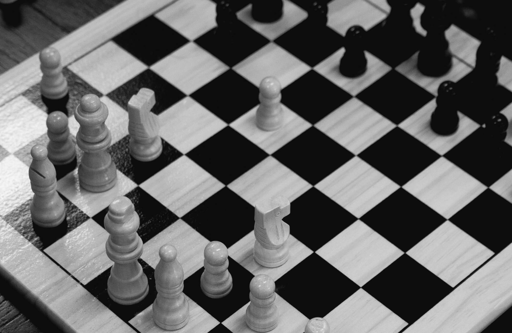 Close-up of a chessboard in black and white, with wooden chess pieces strategically placed, highlighting the game's intricate strategy.