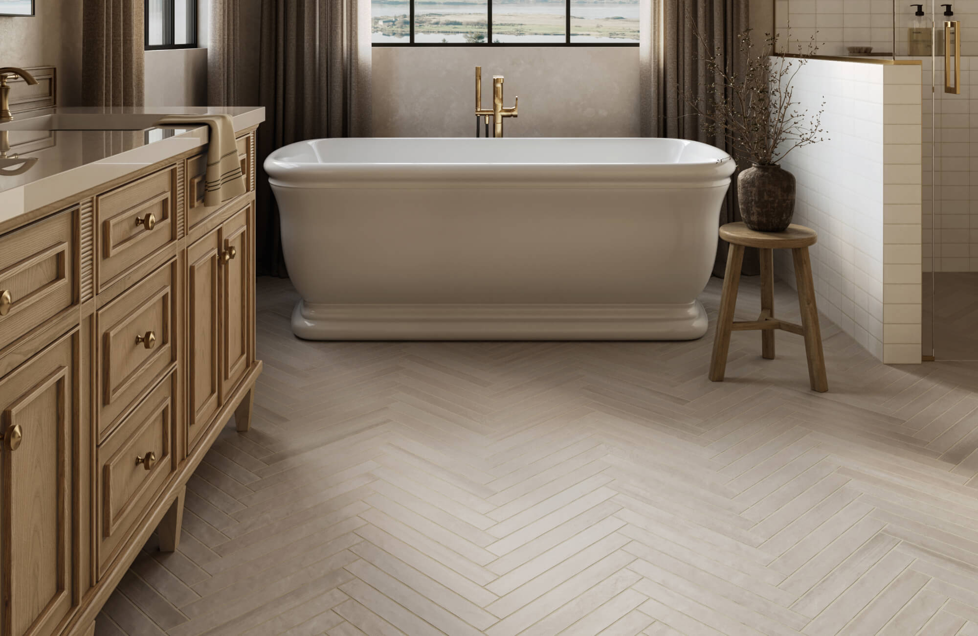 Elegant bathroom with light herringbone floor tiles, freestanding tub, brass fixtures, and warm natural wood cabinetry.