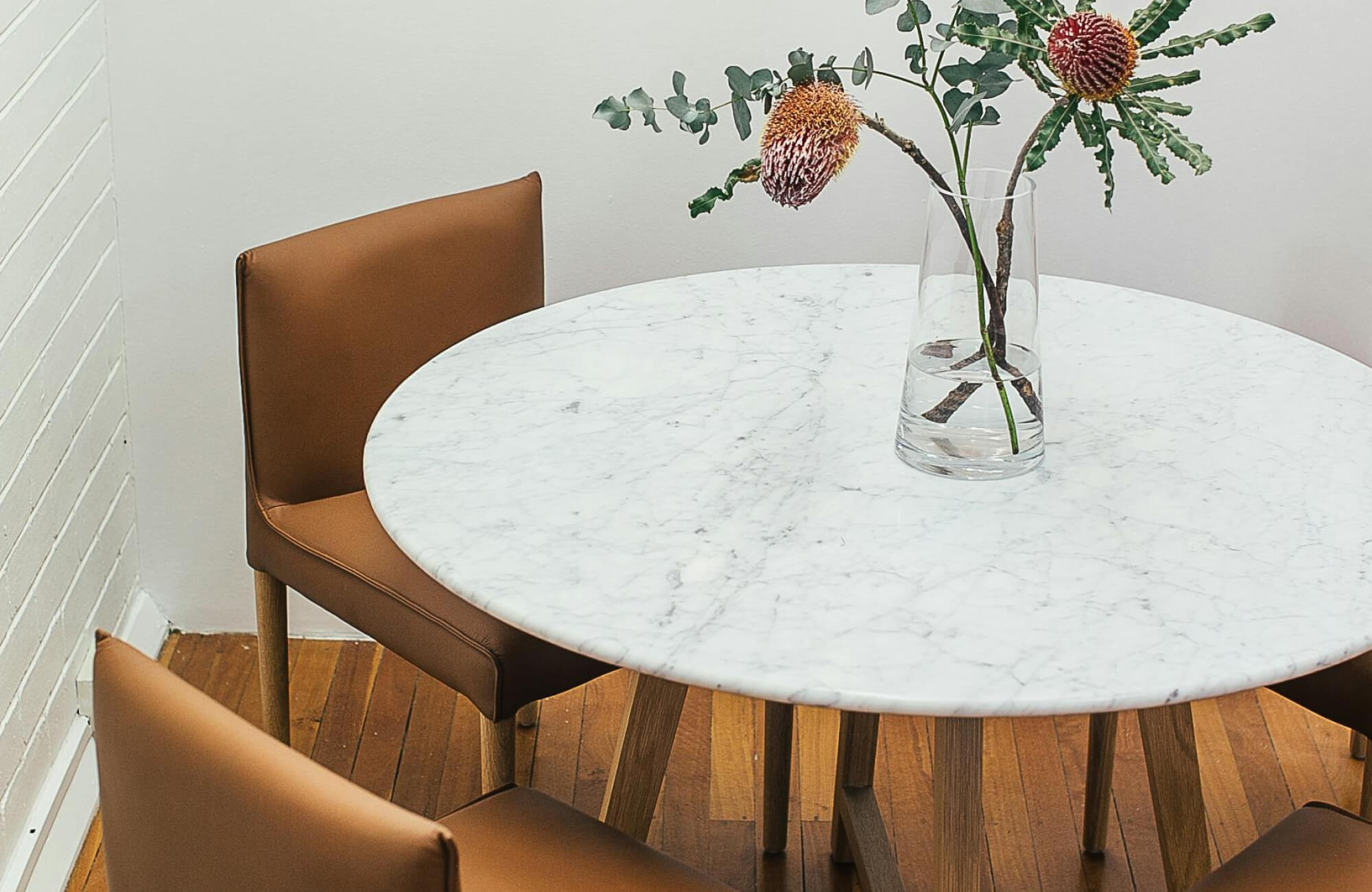 null A round white marble dining table with soft veining surrounded by tan chairs in a cozy corner dining space.