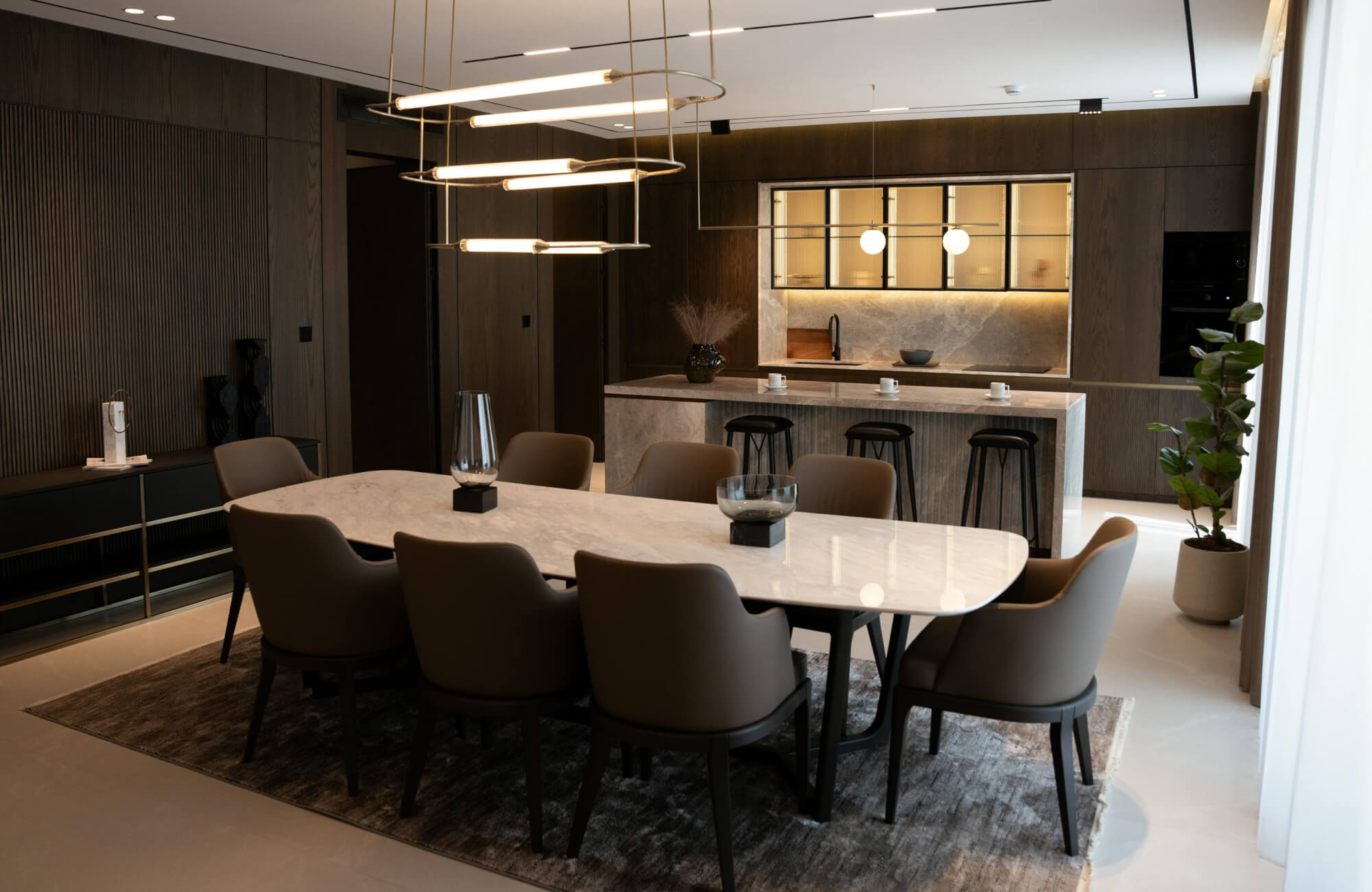 null A long marble dining table in a sophisticated dining room with warm lighting and upholstered chairs.