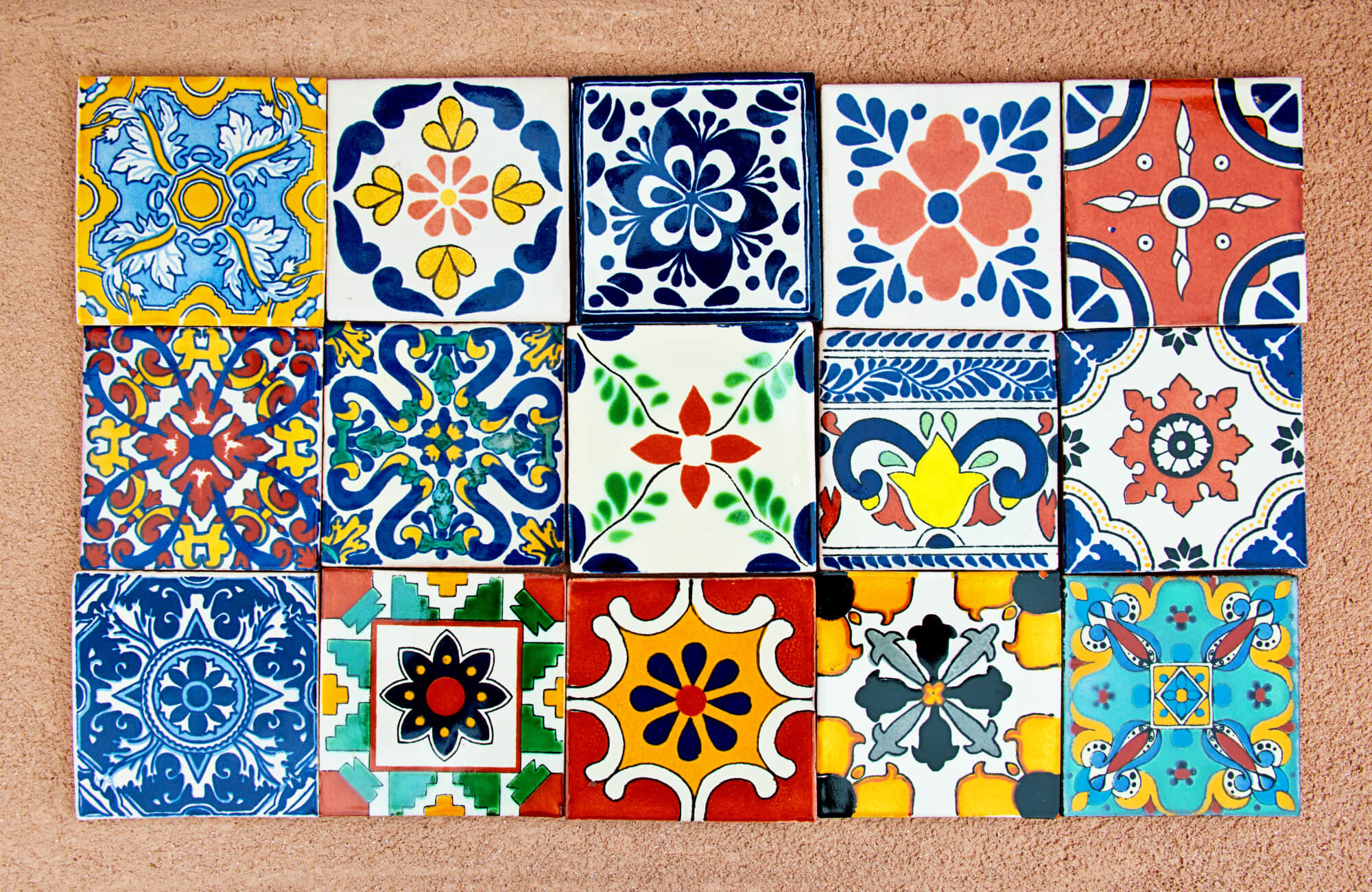 Colorful assortment of decorative ceramic tiles with intricate, hand-painted patterns arranged in a grid on a textured surface.