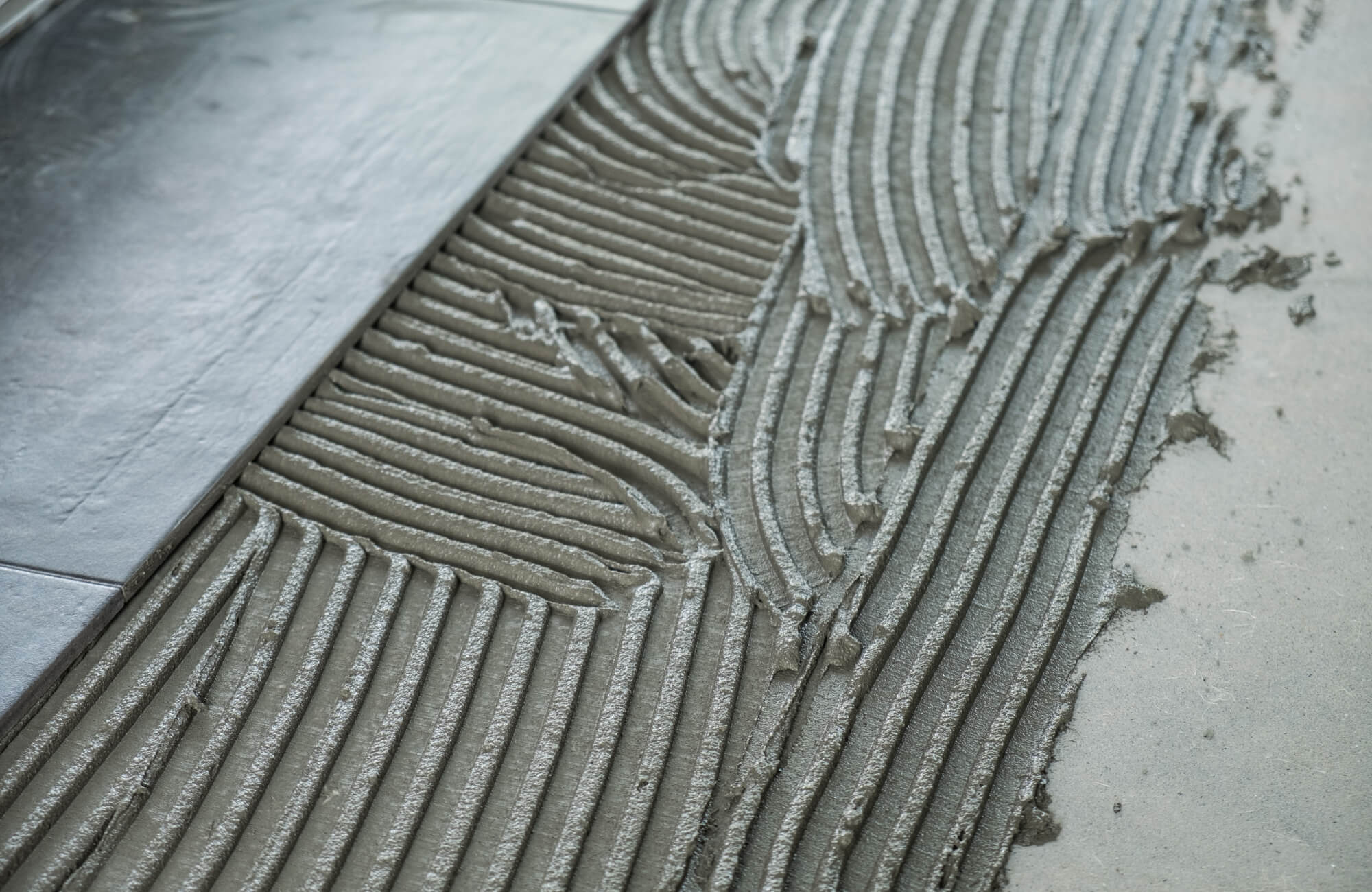 Close-up of ceramic tile being installed with notched trowel lines in thin-set mortar on a prepared bathroom subfloor surface.