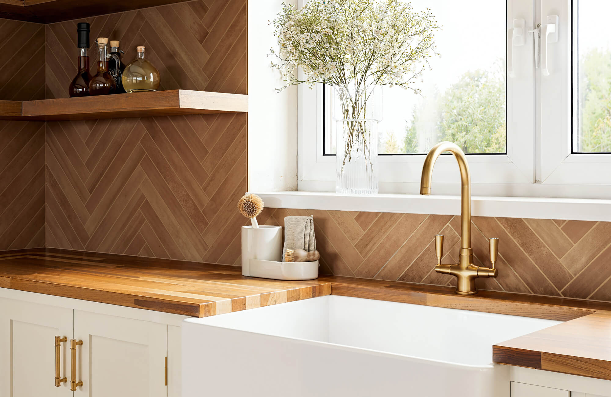 Bright kitchen corner featuring tan herringbone wall tiles, gold fixtures, and natural wood accents for a cozy, refined look.