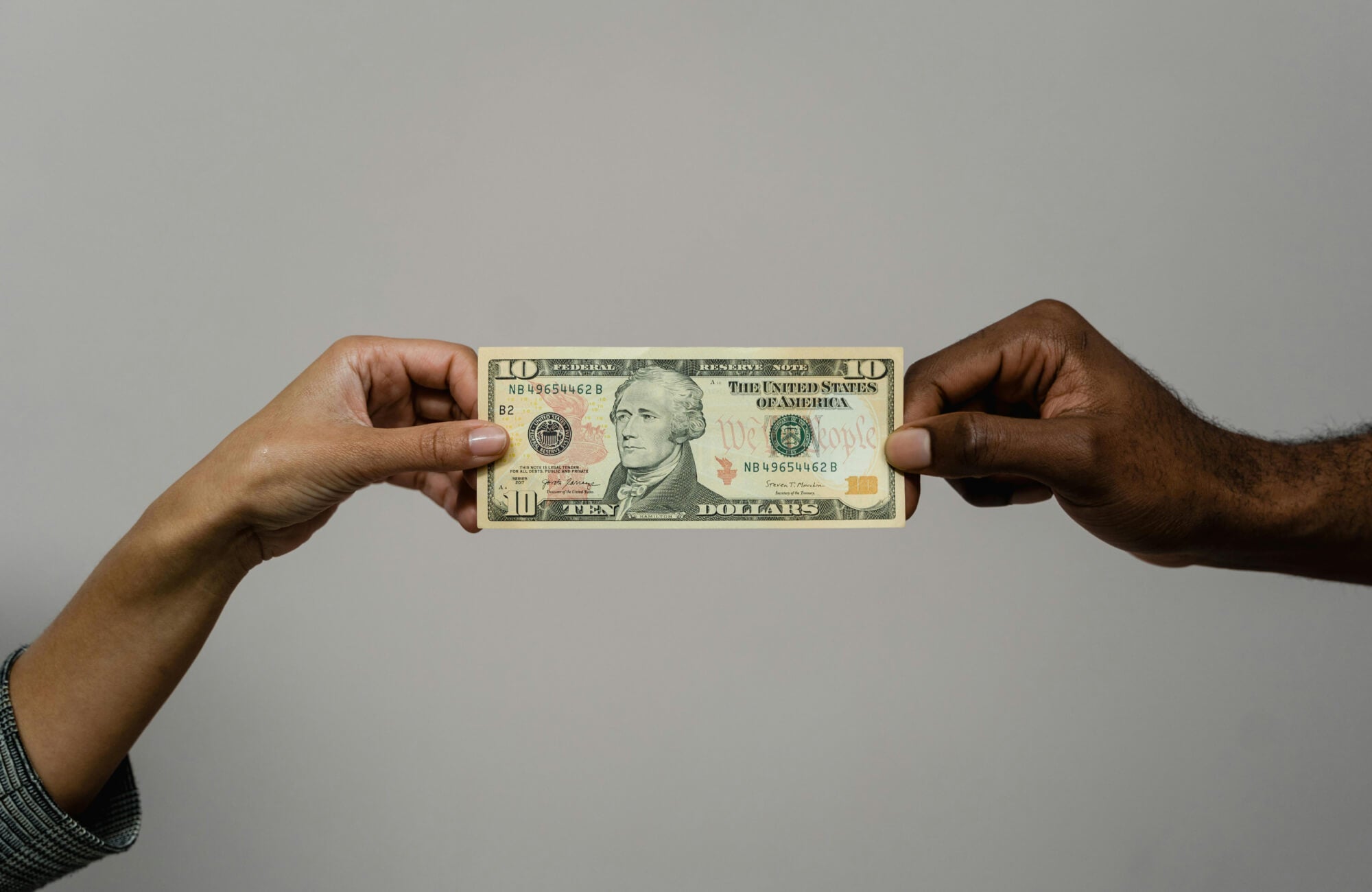 Close-up of two people sharing a ten-dollar bill, representing budgeting, pricing, or expense discussion.