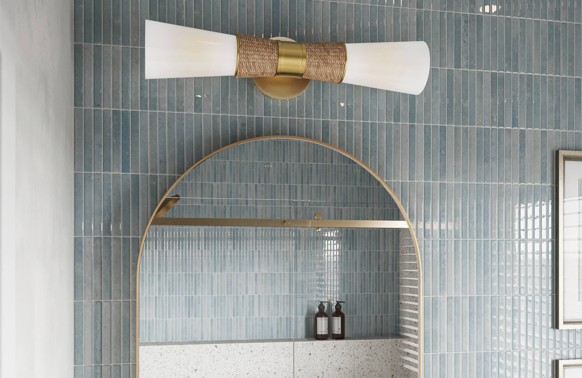 Close-up of a bathroom with vertical blue wall tiles, brass-framed arched mirror, and modern double-cone vanity light.