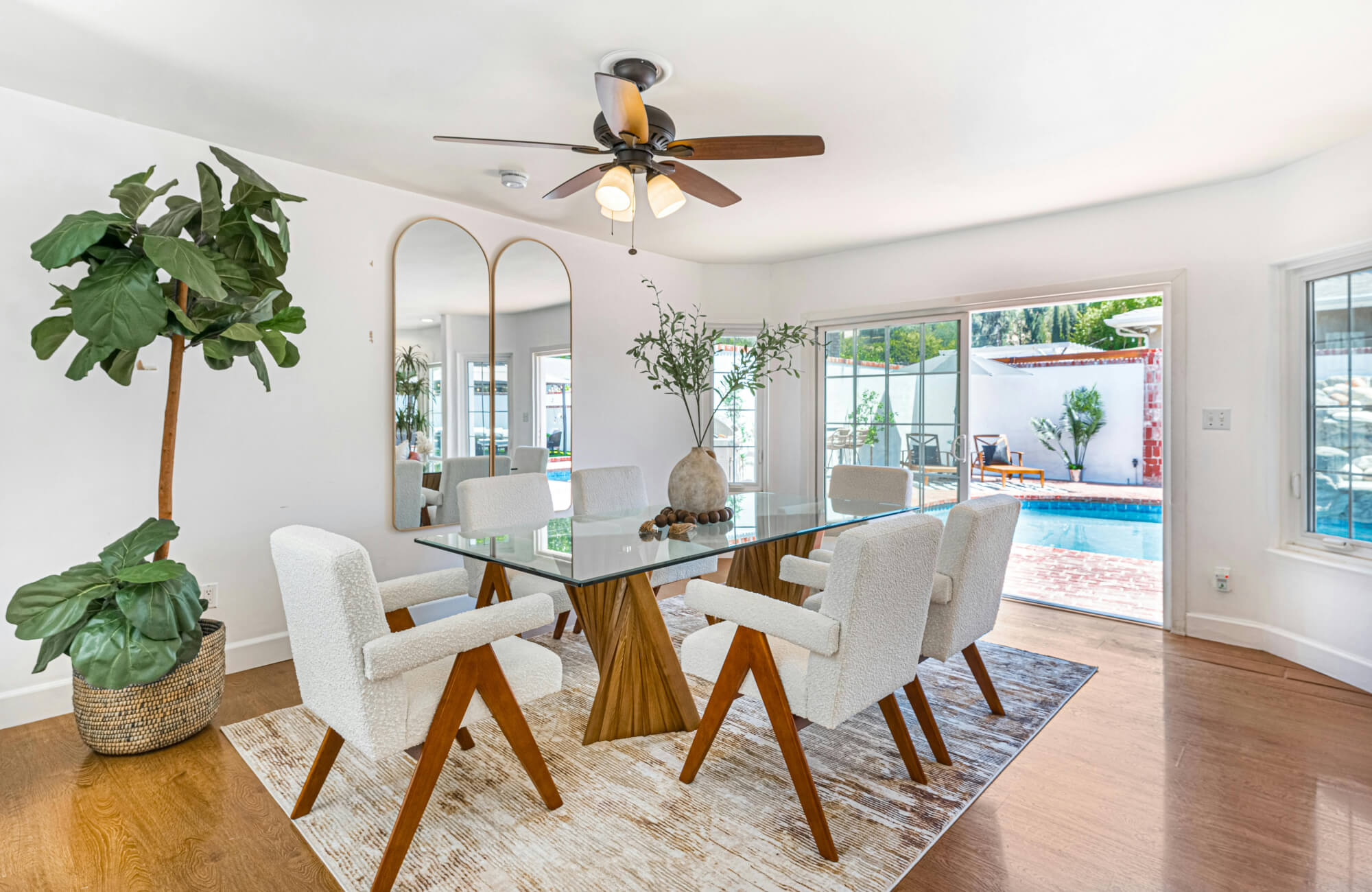 Tall arched mirrors reflecting a bright dining room with a glass table and white chairs