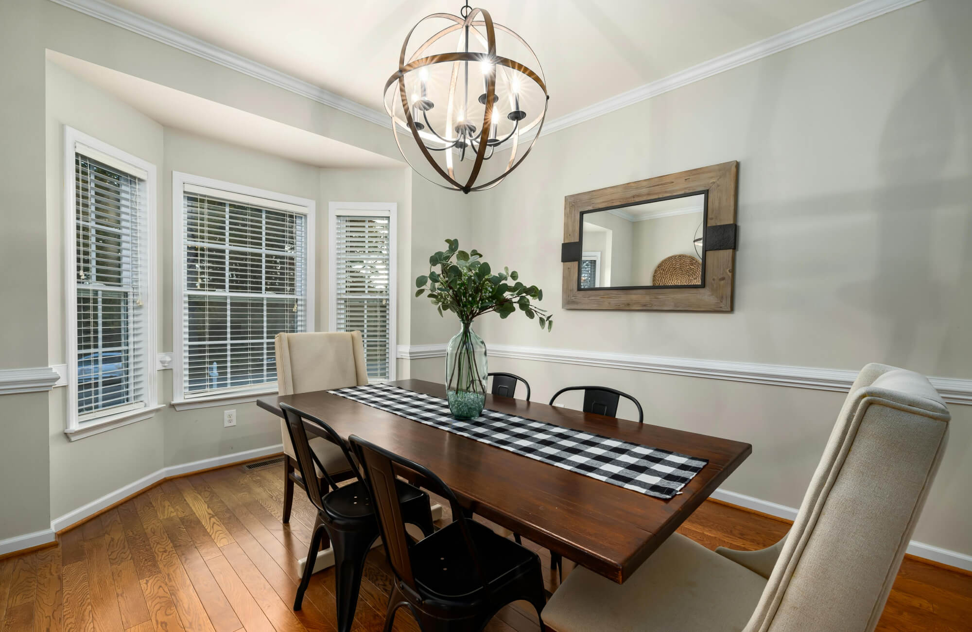 Rectangular wood-framed mirror reflecting a light-filled dining room with bay windows
