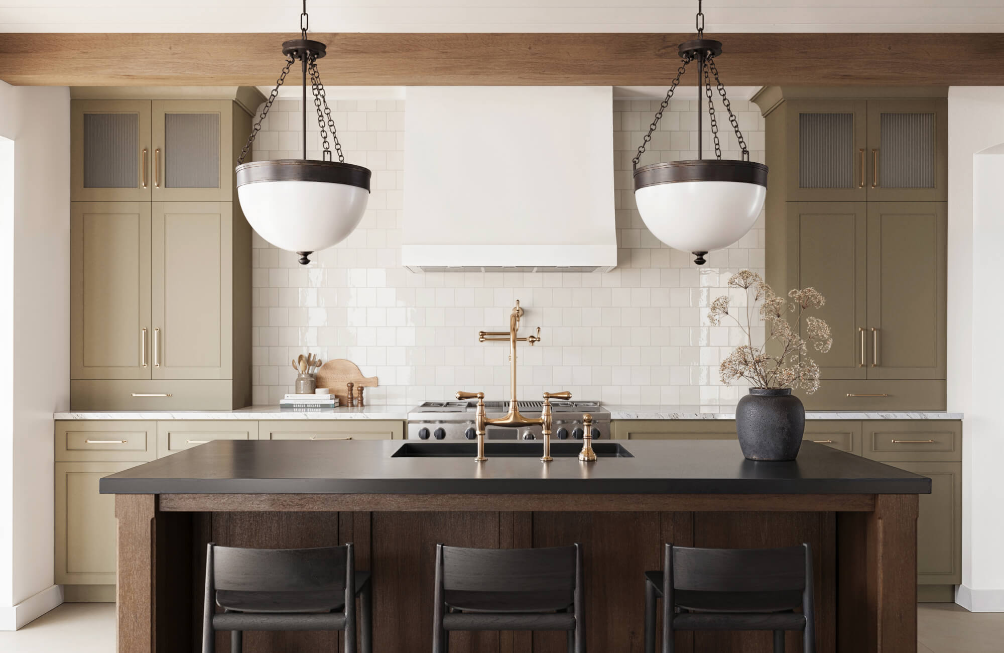 Classic yet modern kitchen showcasing statement bowl-style kitchen pendant lighting suspended over a dark island, complemented by sage cabinetry, white subway tile backsplash, and warm brass fixtures for a refined, timeless look.