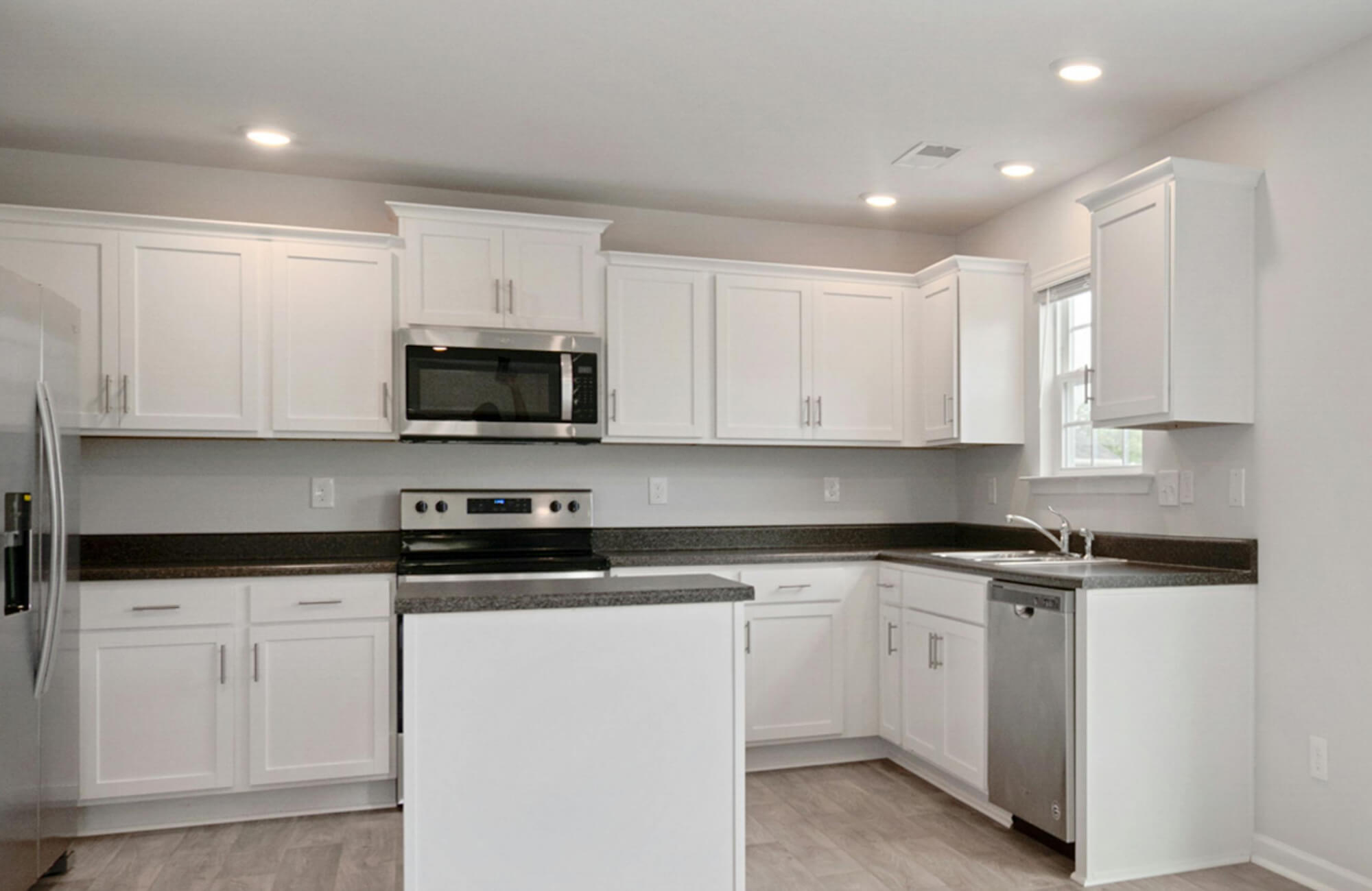 Bright white kitchen with recessed ceiling downlights providing even task illumination over the island and perimeter countertops, creating a clean, functional, and well-lit workspace.