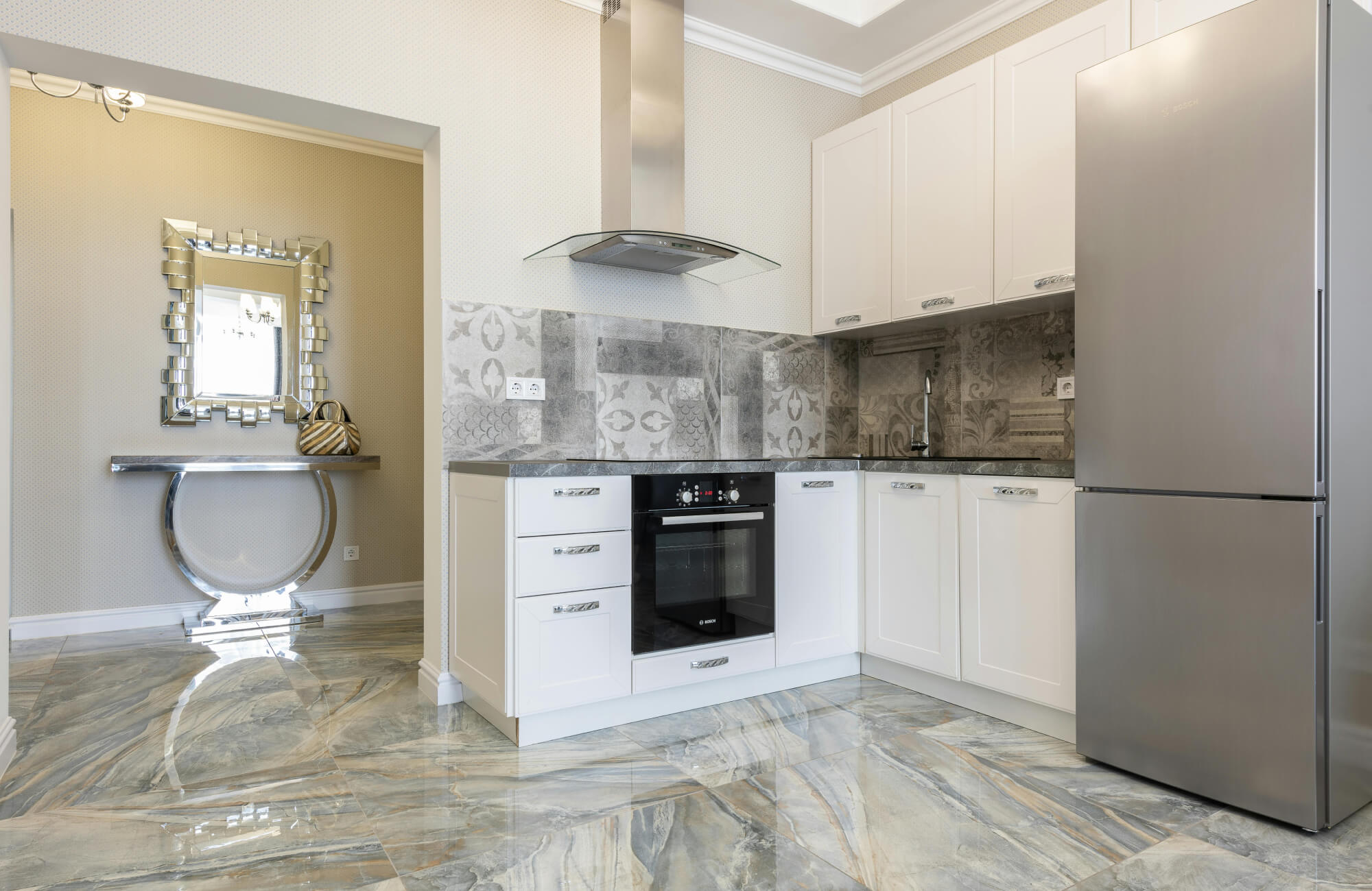 Modern kitchen with glossy marble flooring in gray and beige tones, paired with decorative patterned backsplash tiles and sleek white cabinetry.