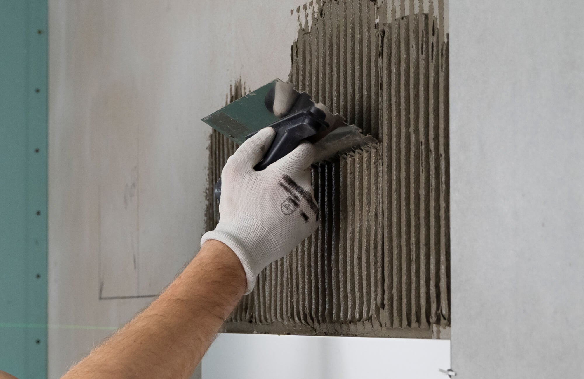 null A worker spreads tile adhesive on a wall using a notched trowel, creating even grooves for a secure and professional marble tile installation.