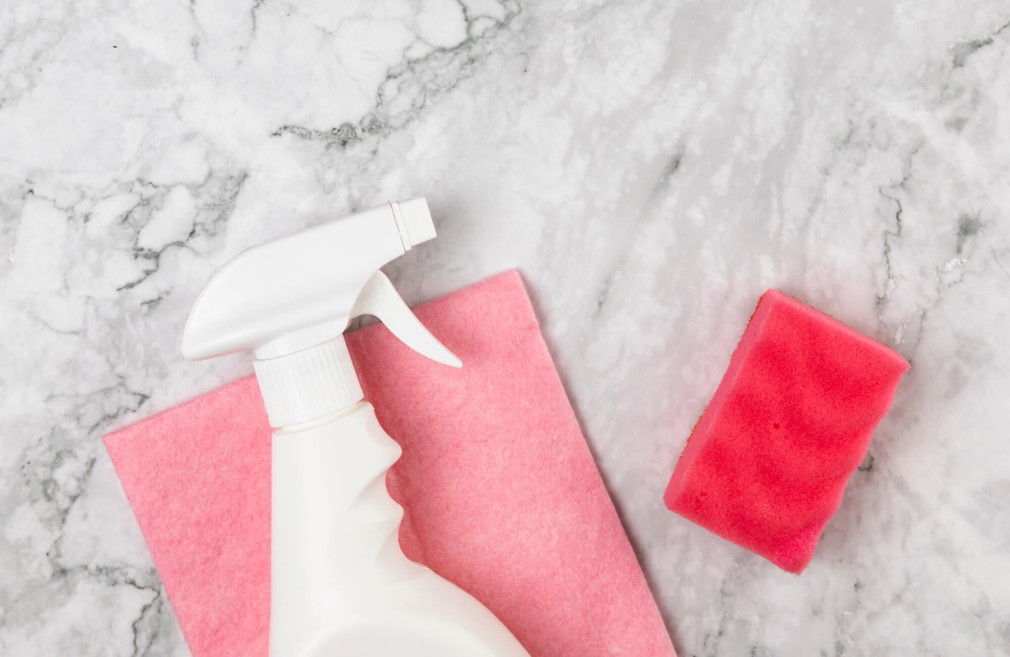 null A spray bottle, sponge, and cloth rest on a polished white marble surface with gray veining, ready for cleaning and maintenance.