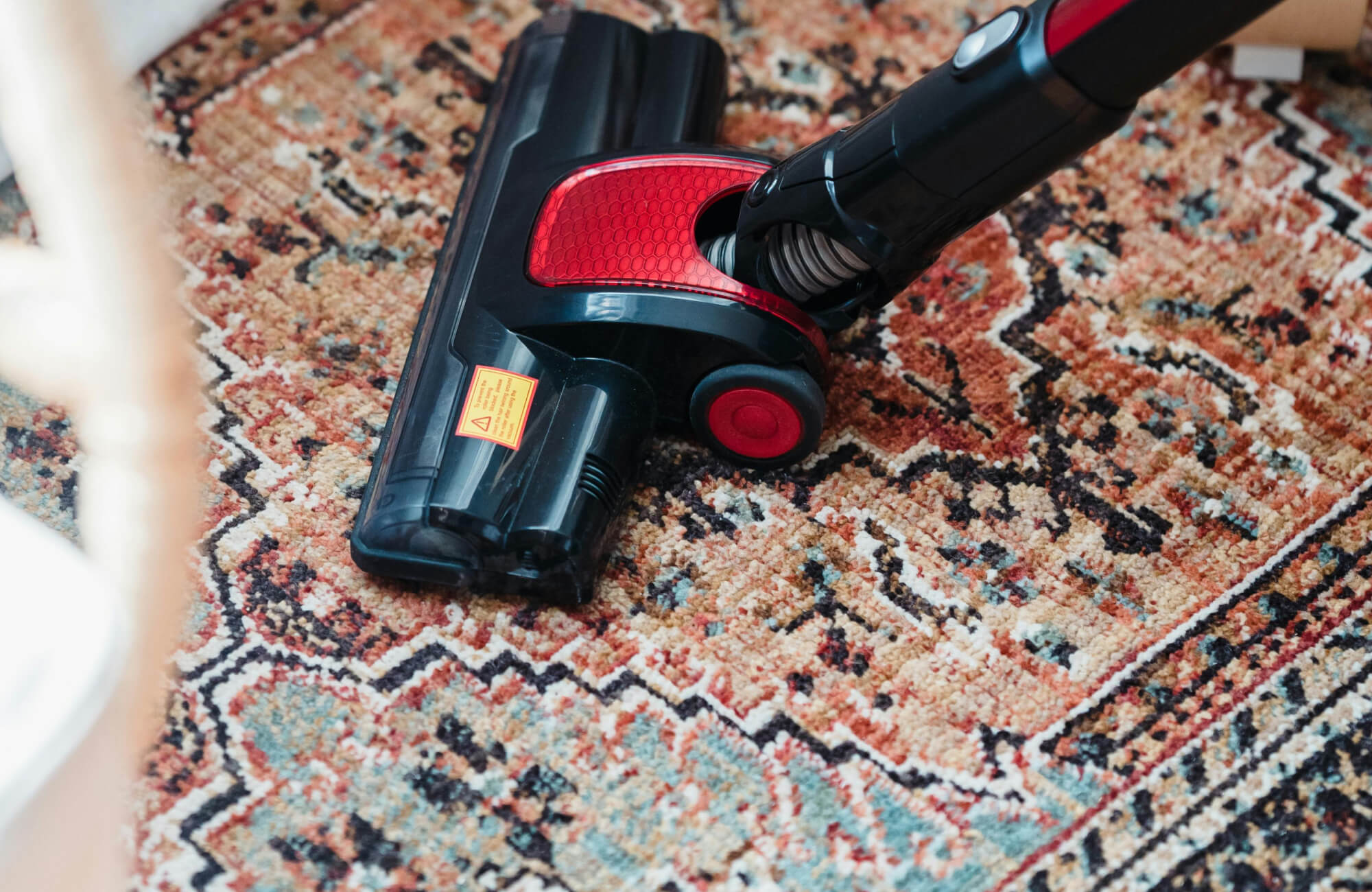 Vacuum cleaning a richly patterned vintage-style polyester rug in warm terracotta and teal tones.