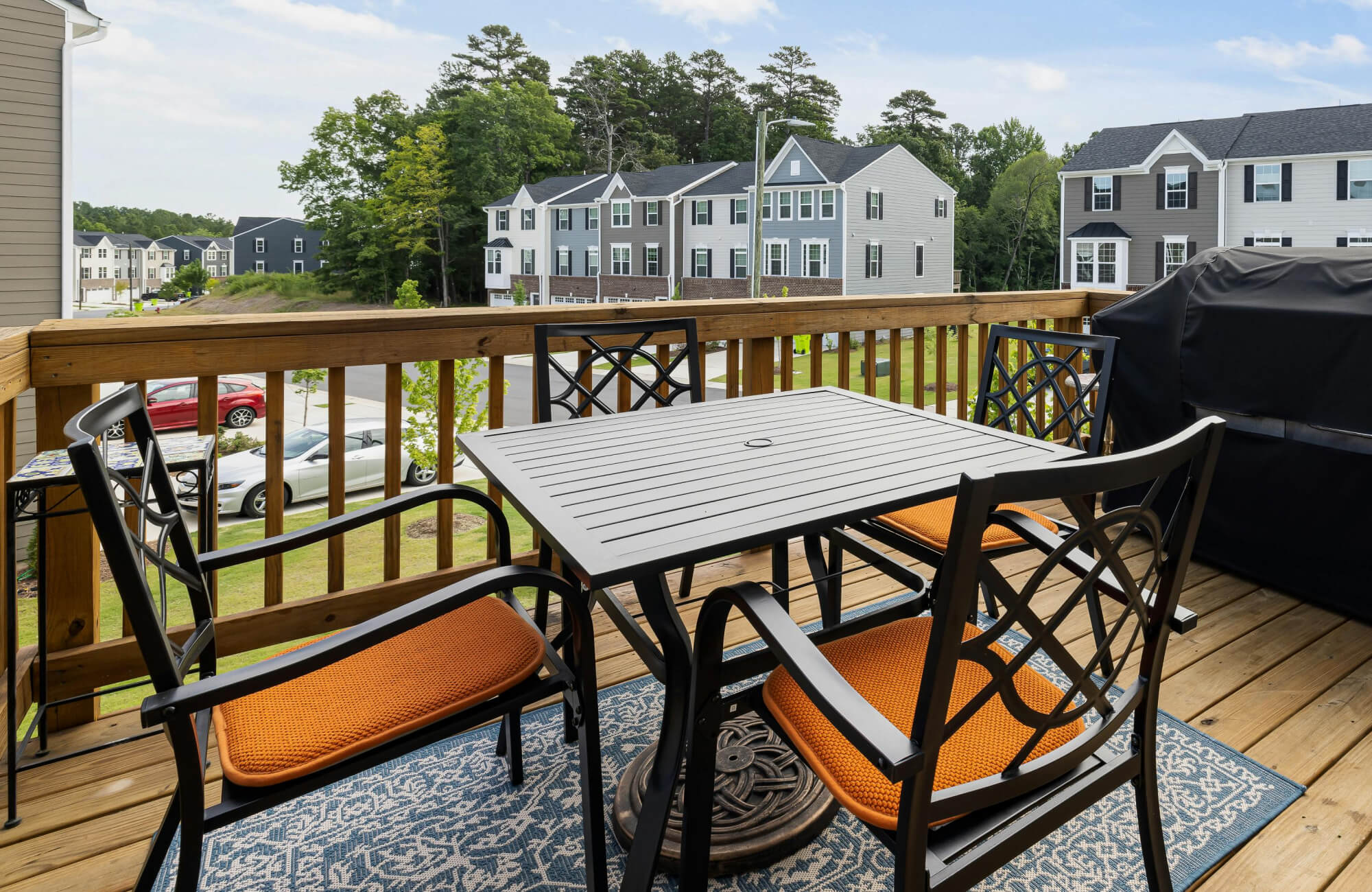 Modern patio setup with black metal dining set and orange cushions atop a blue patterned polypropylene outdoor rug.