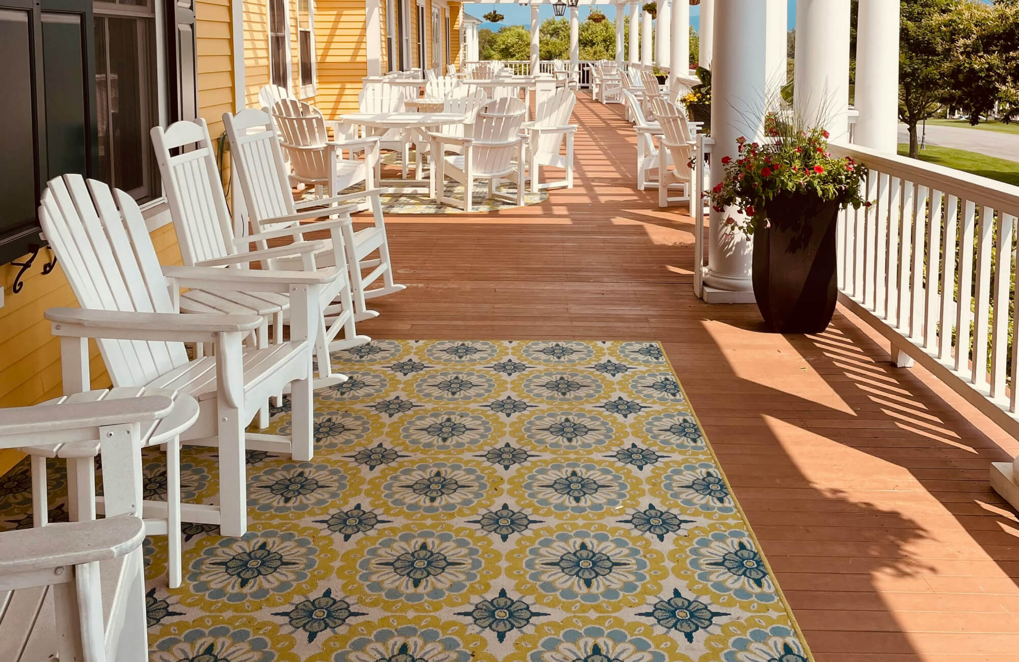 Charming porch with white Adirondack chairs and a floral-patterned polypropylene rug in yellow, teal, and cream tones.