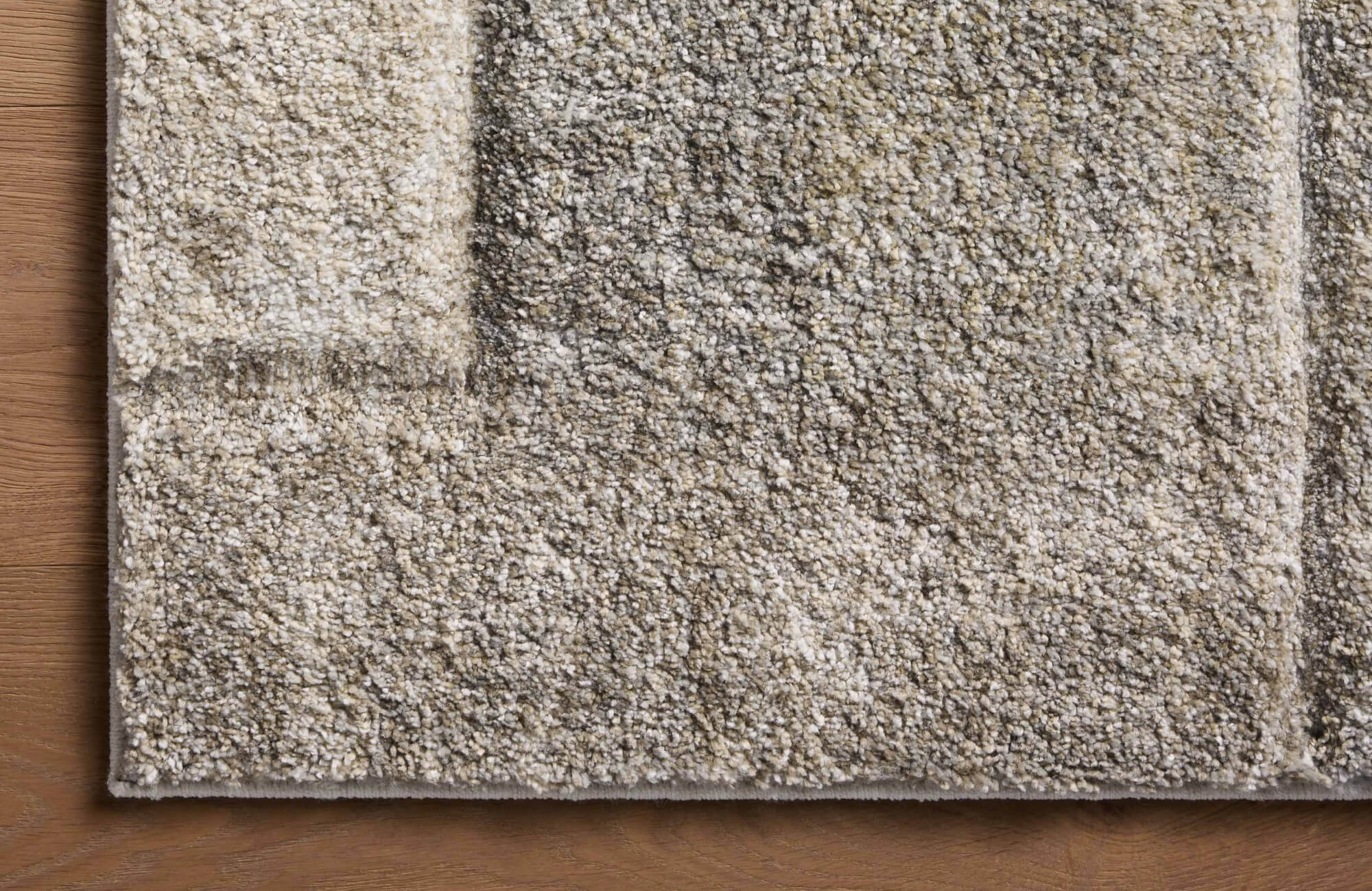 Close-up of a taupe and stone polypropylene rug with a soft pile, subtle geometric pattern, and bound edge on wood flooring.
