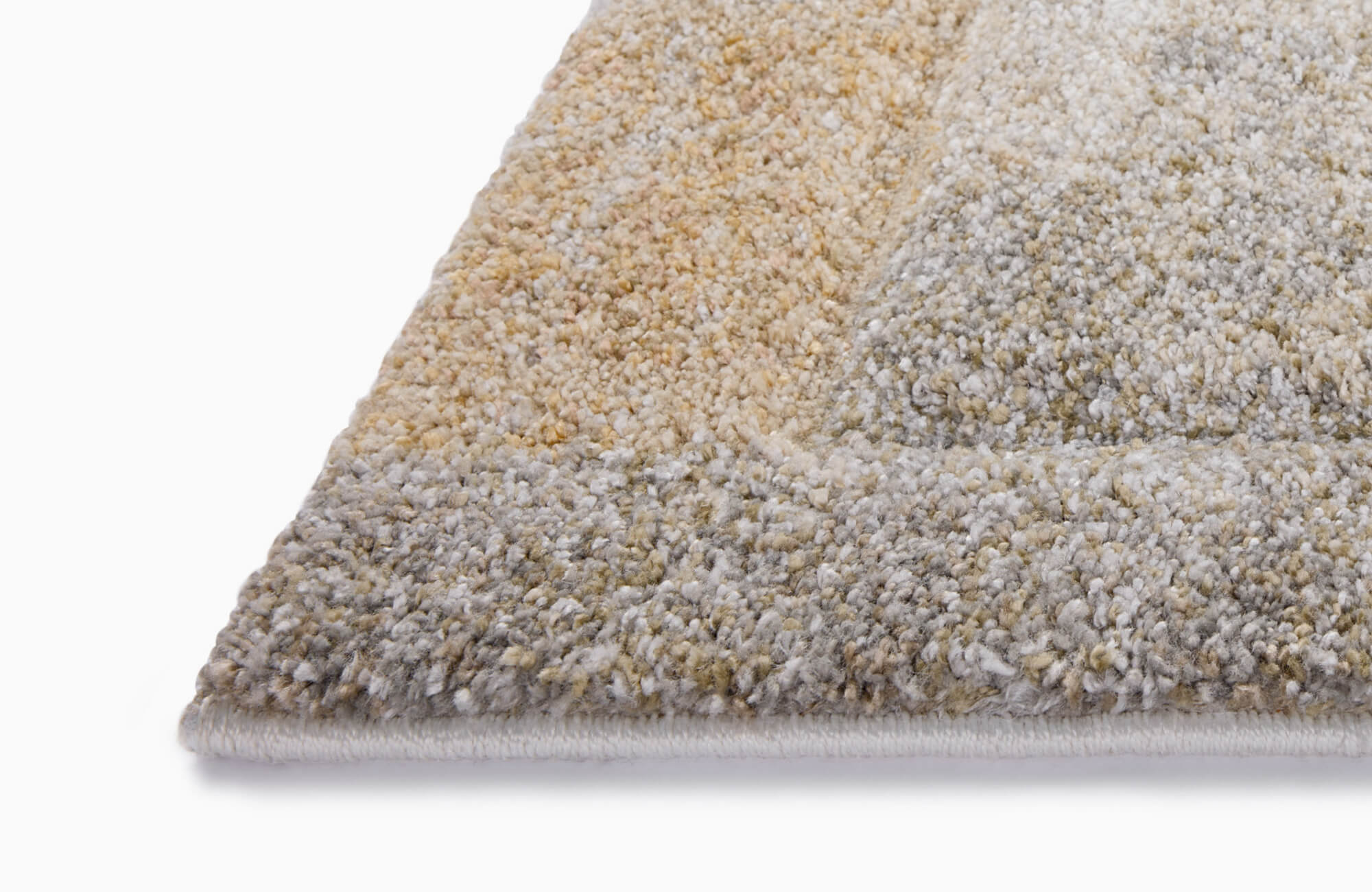 Angled detail of a plush polypropylene rug corner showing cream, beige, gray, and muted gold fibers with a raised geometric pattern.