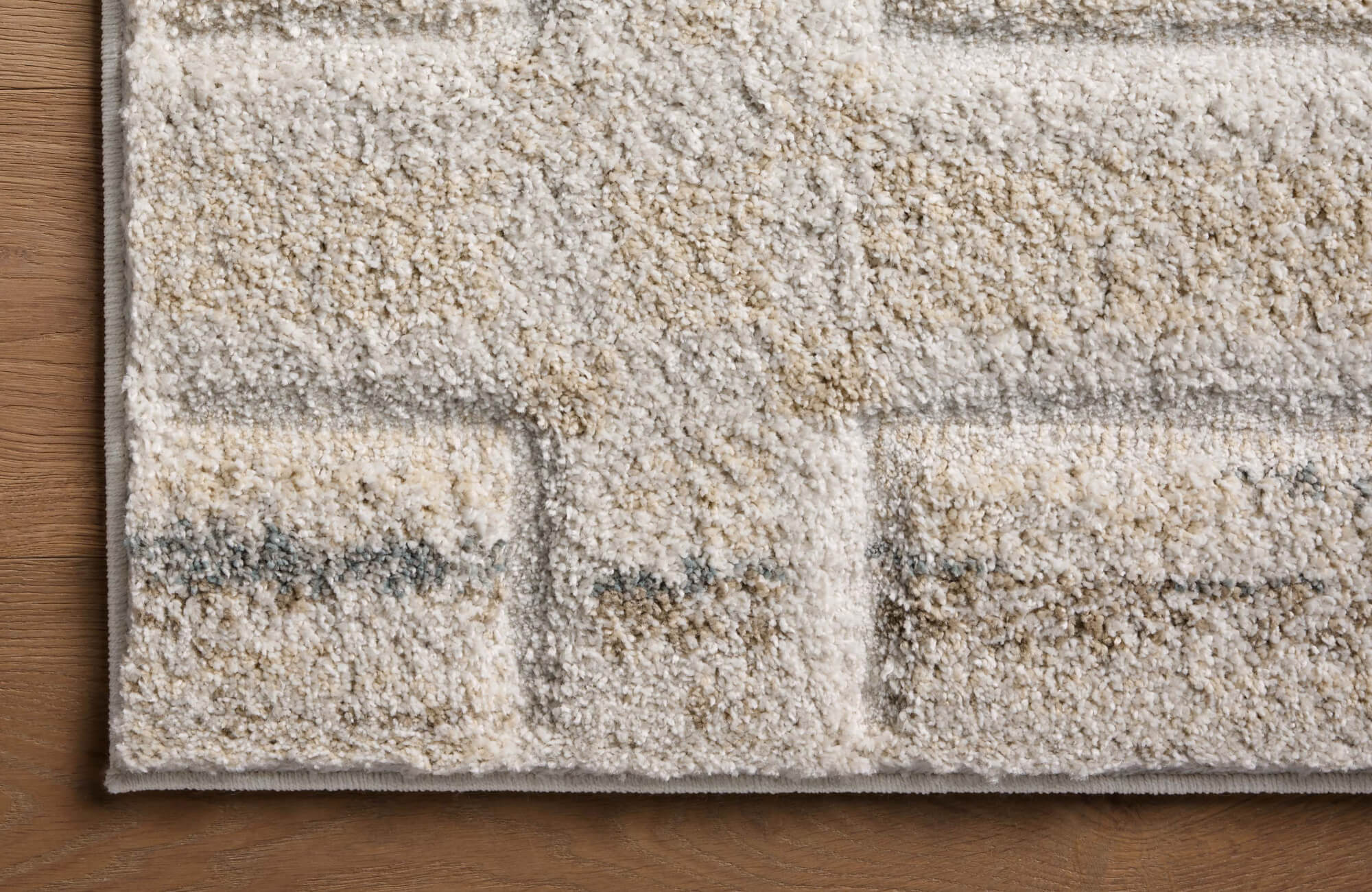 Close-up of a cream and taupe polypropylene rug with soft pile texture, tonal geometric lines, and a finished edge on wood flooring.