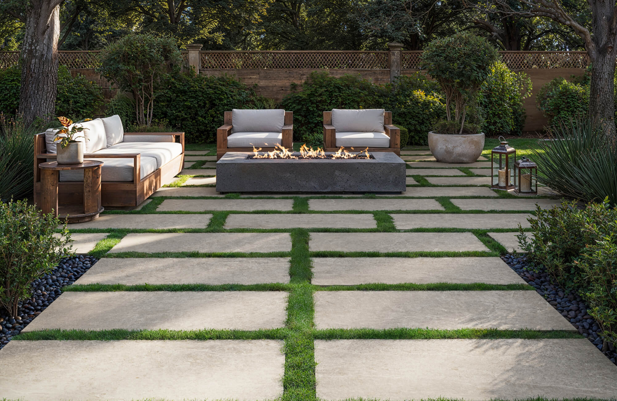 Spacious patio with large stone look porcelain pavers set in lush grass, framing a modern fire pit and wooden outdoor seating.