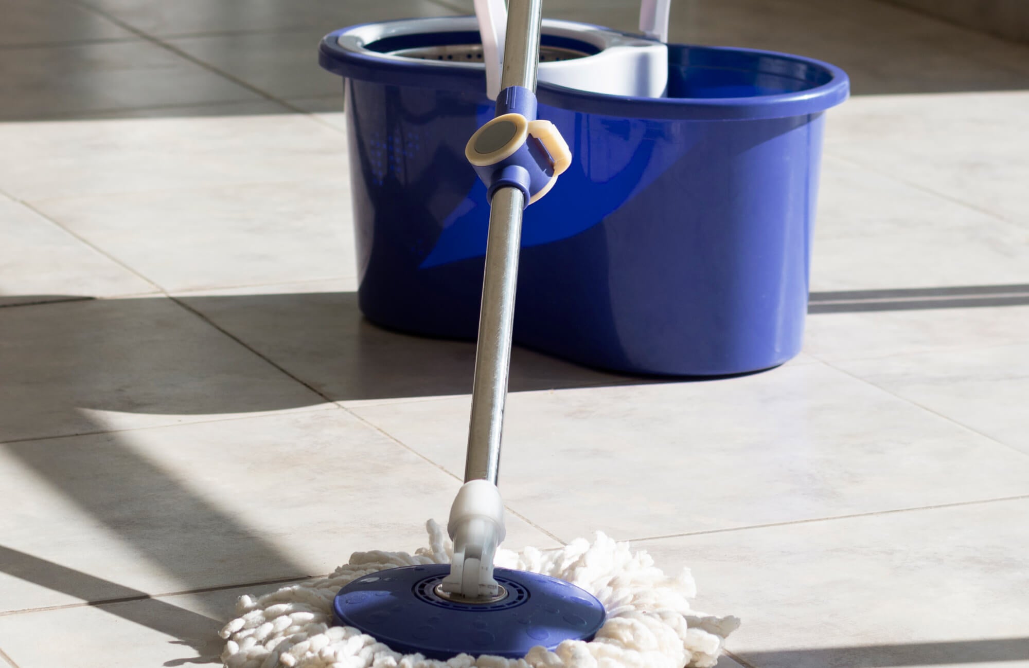 Wet mopping in progress on pale stone tiles, with a bucket nearby, illustrating everyday bathroom floor maintenance and how natural stone surfaces are cleaned.