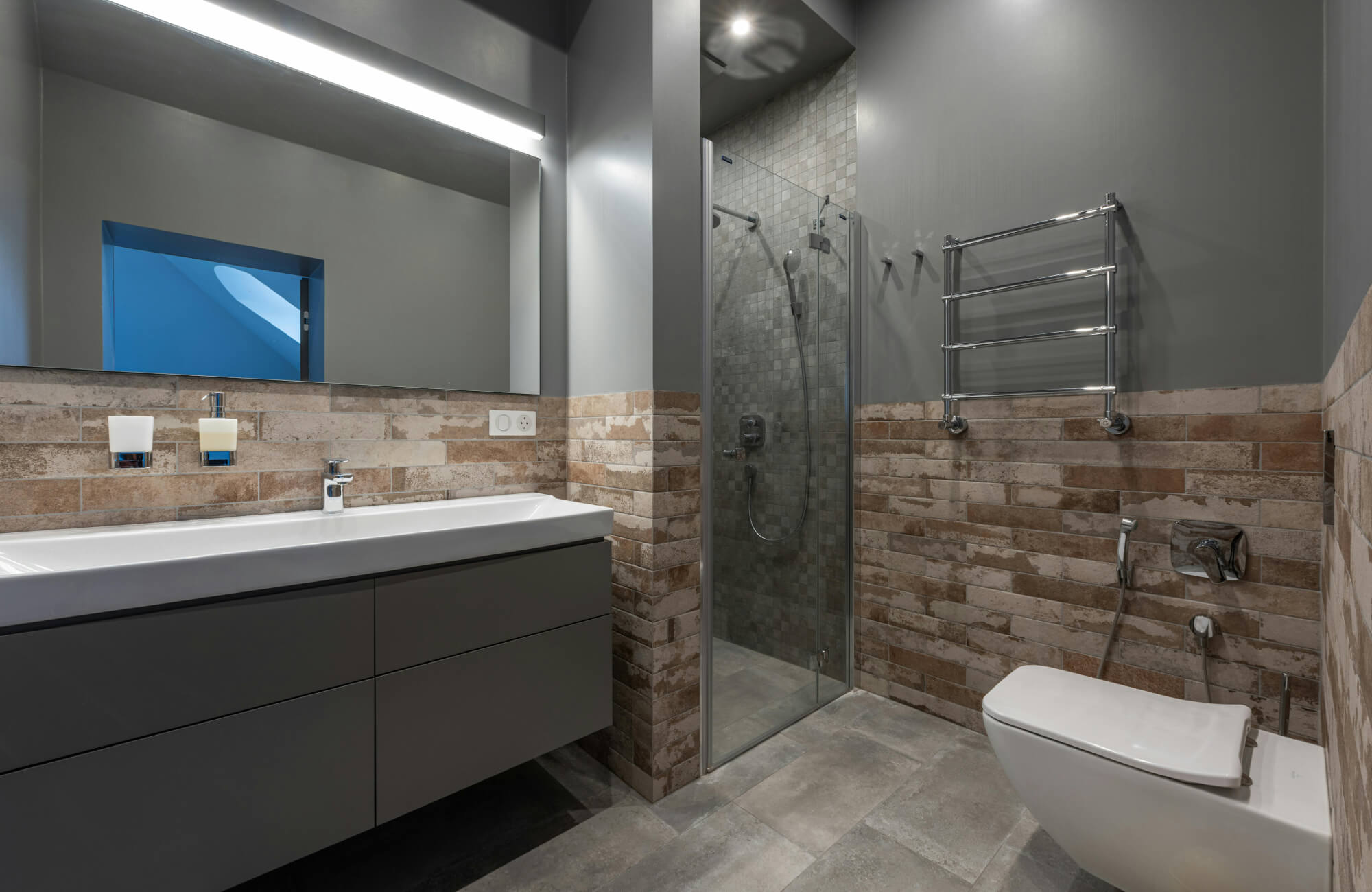 A contemporary bathroom featuring slate-style flooring and stone wall tiles paired with a glass shower, highlighting practical surface choices for daily bathroom use.