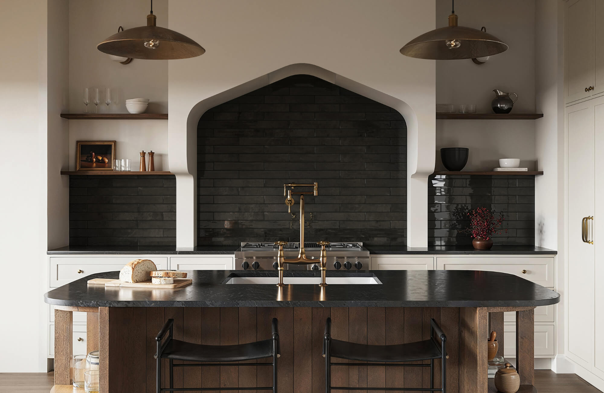 Modern kitchen with a glossy black subway tile backsplash, arched range hood, brass faucet, and dark stone island with wood paneling.