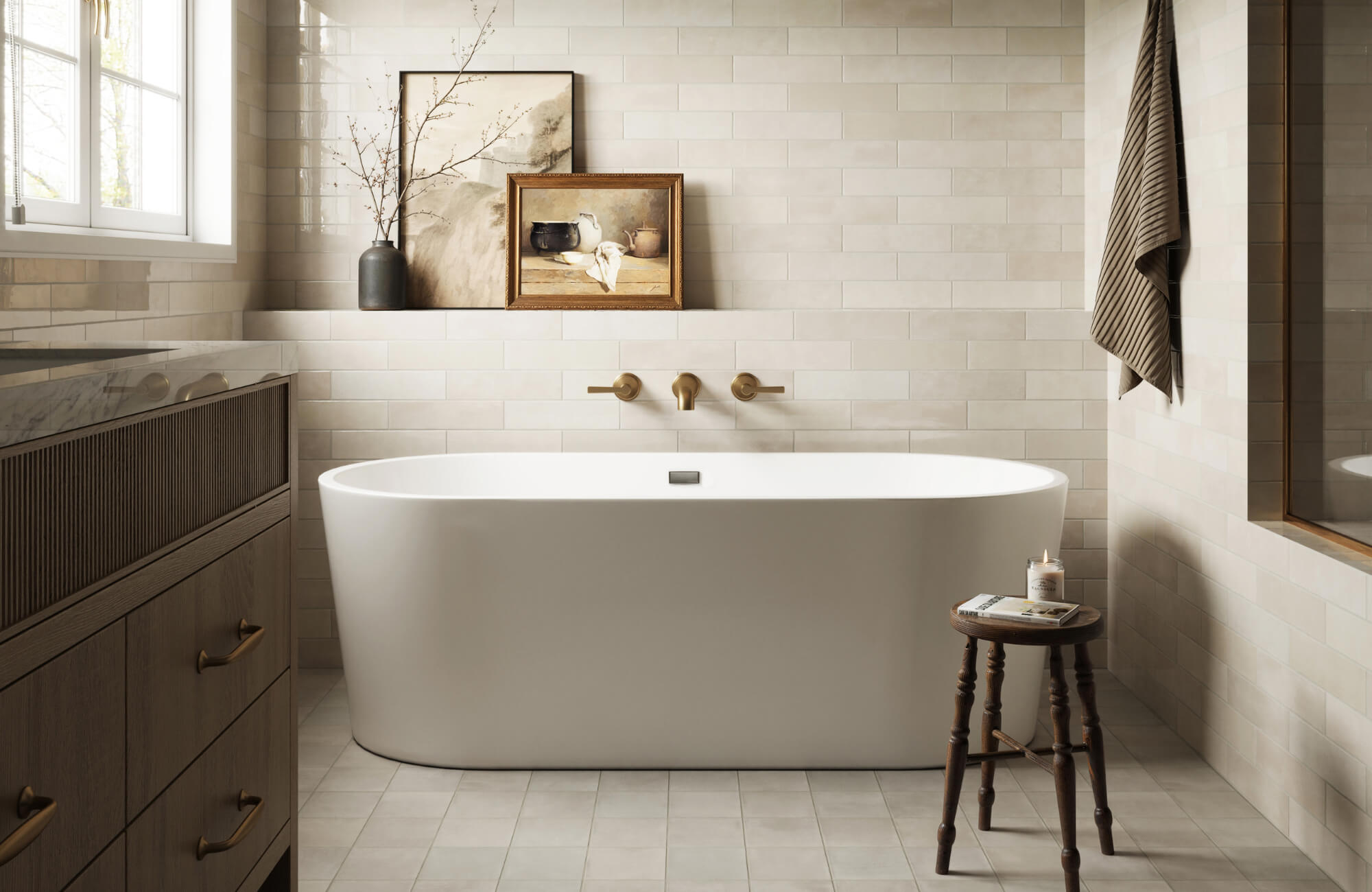 Serene bathroom with beige subway tile walls, a freestanding tub, brushed gold fixtures, wood vanity, and a small stool with candle and book.