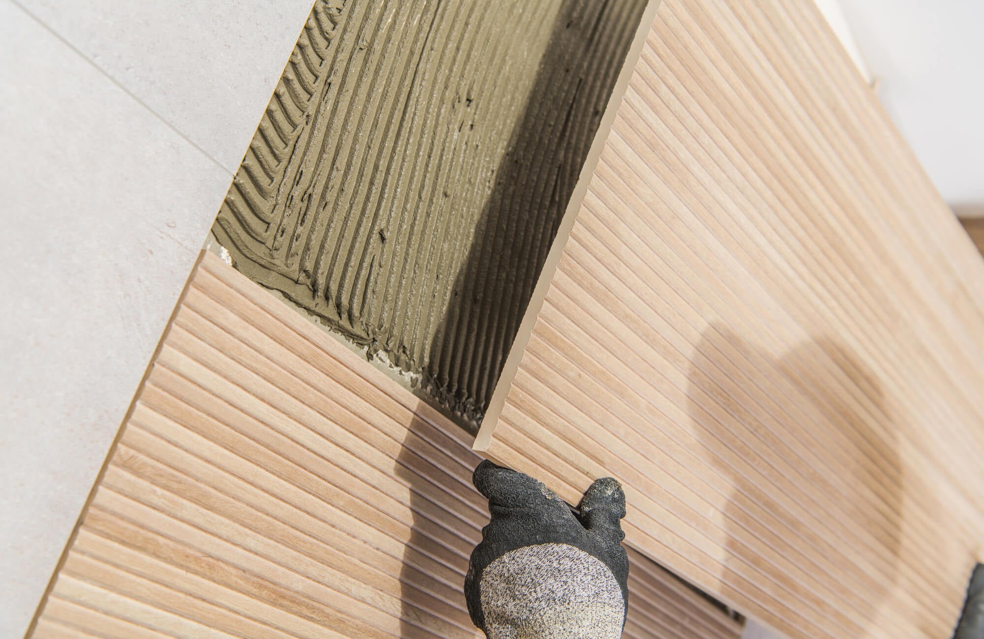 Close-up of a gloved hand installing wood look tile with thin-set mortar, highlighting the textured surface and precision placement.