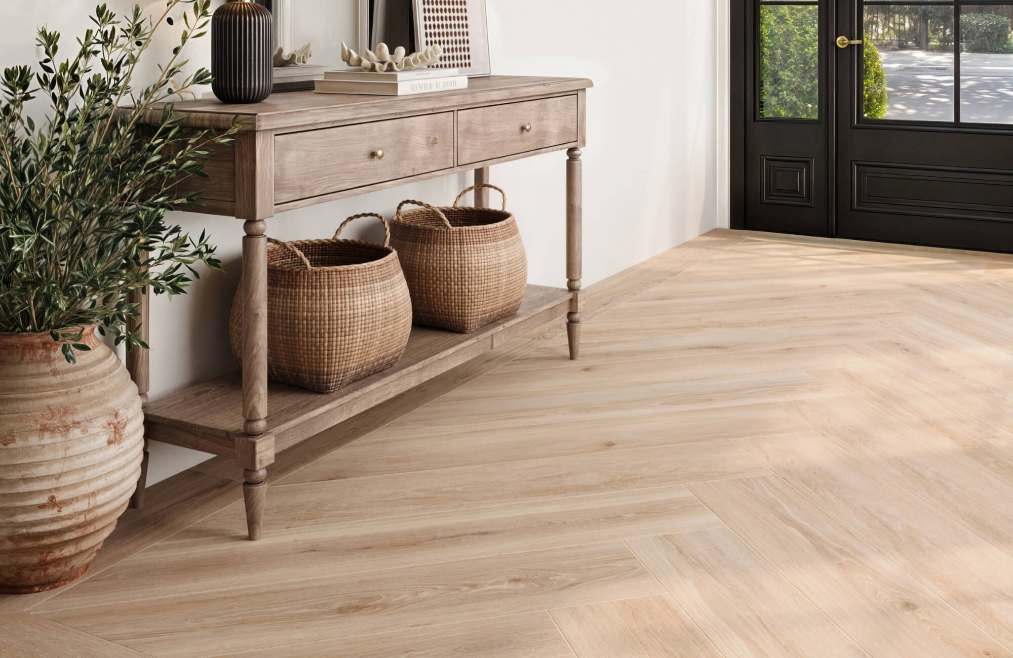 Entryway with light wood look tile flooring in a herringbone pattern, rustic console table, woven baskets, and large decorative planter.