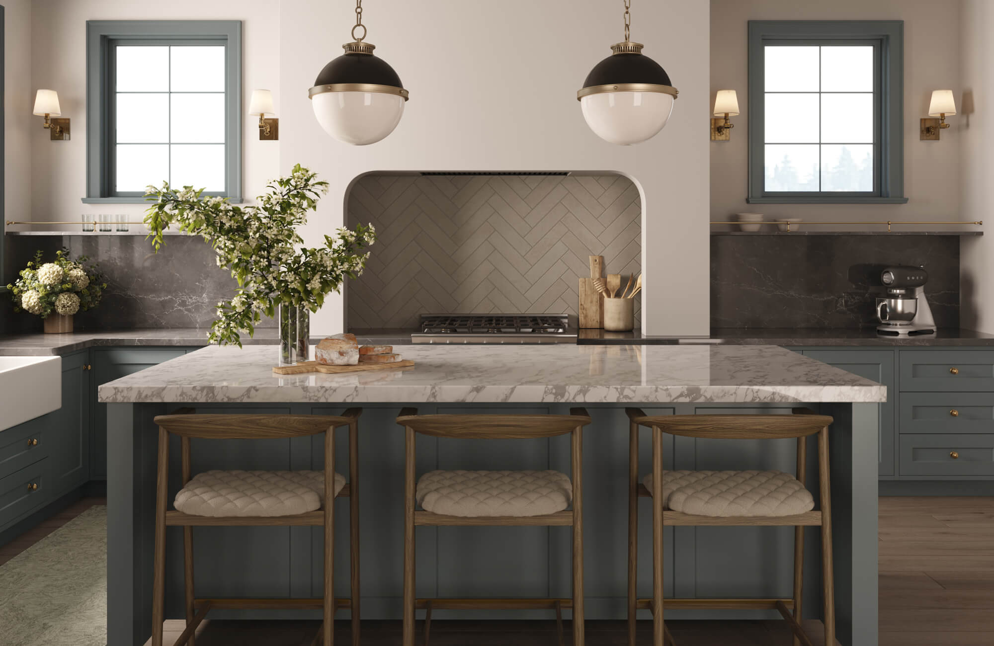 Classic kitchen design featuring a marble-topped island with upholstered stools, muted blue cabinetry, a herringbone tile backsplash framed by an arched niche, and elegant globe pendant lighting for a refined, balanced aesthetic.