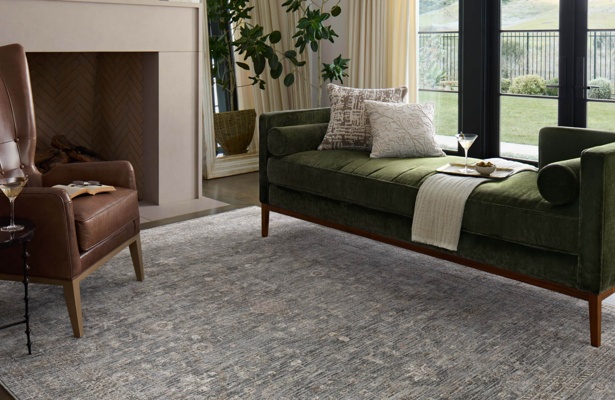 Living room with olive green velvet daybed, brown leather armchair, light gray textured area rug, and large glass doors to patio