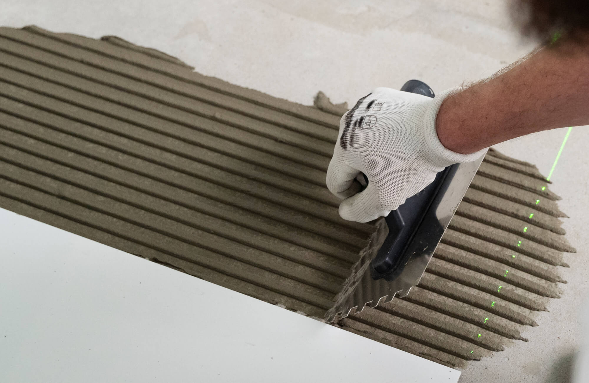 null Precise installation by a gloved hand using a notched trowel to evenly spread tile adhesive, creating clean, consistent ridges that ensure proper alignment and long-lasting structural integrity.