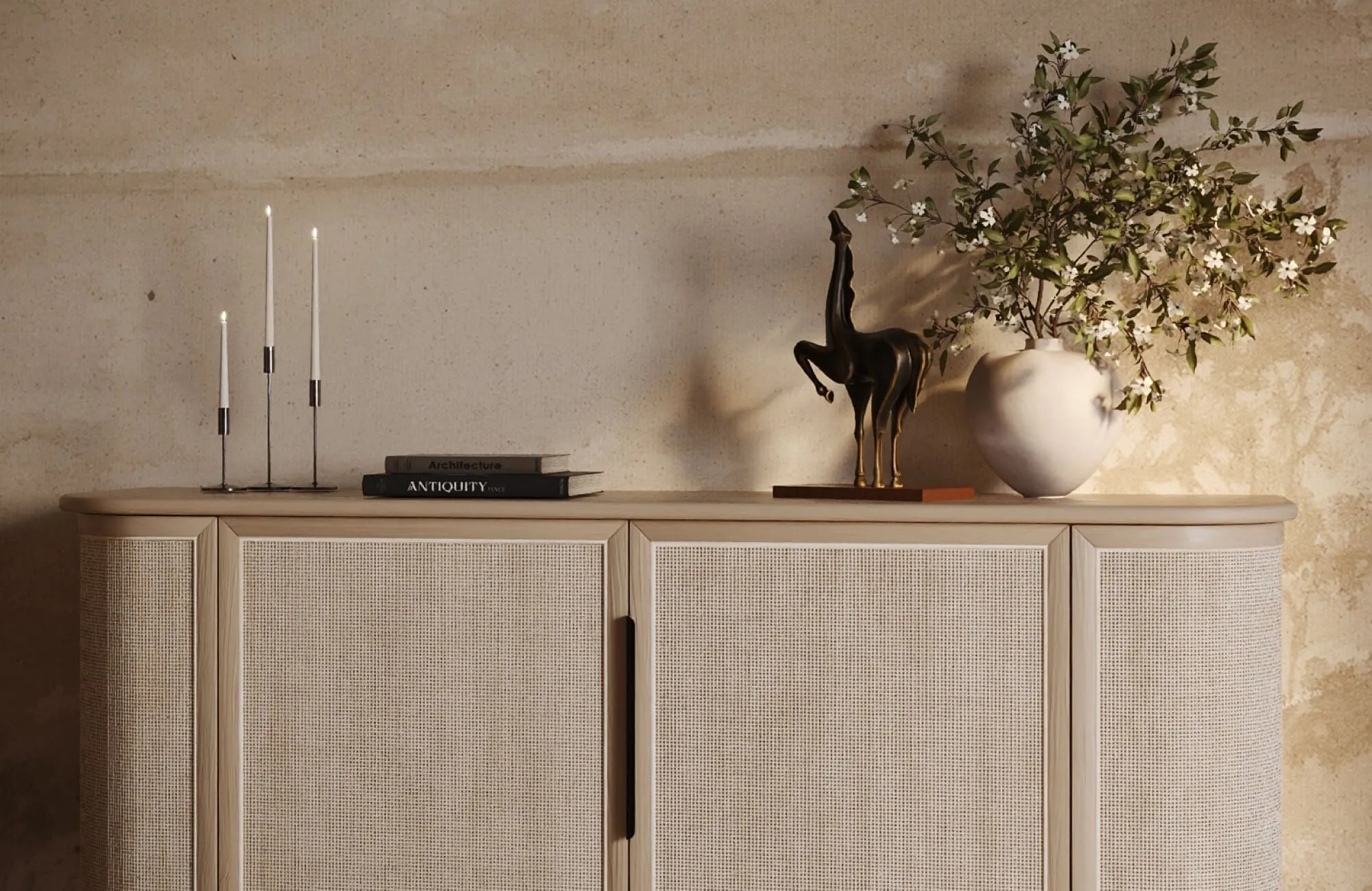 Modern horse sculpture styled on a light woven sideboard in a warm modern living room with candles, books, and a white vase.