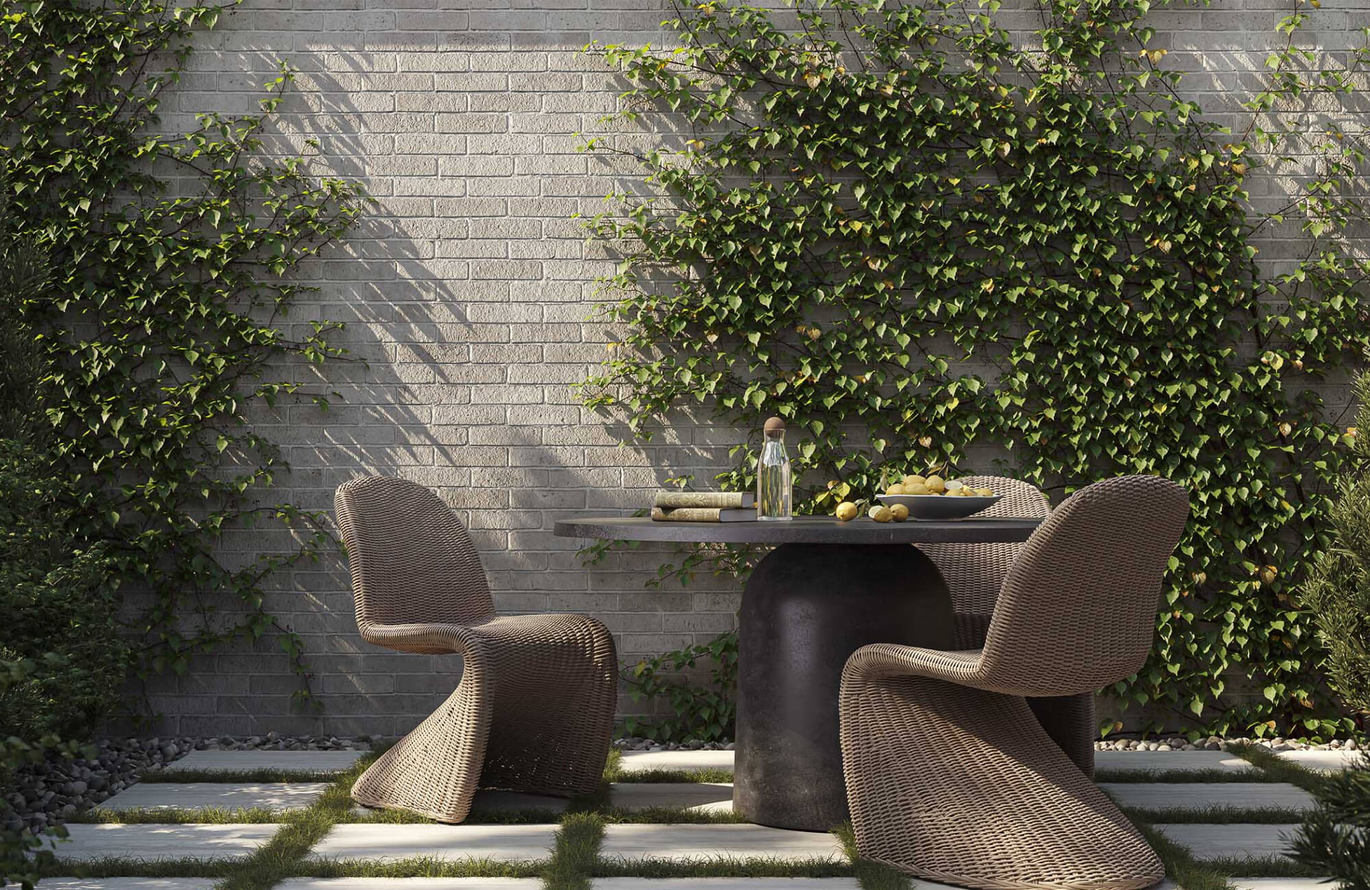 null A pedestal dining table with woven chairs sits on a paved garden terrace against a brick wall accented by climbing vines and soft afternoon light.