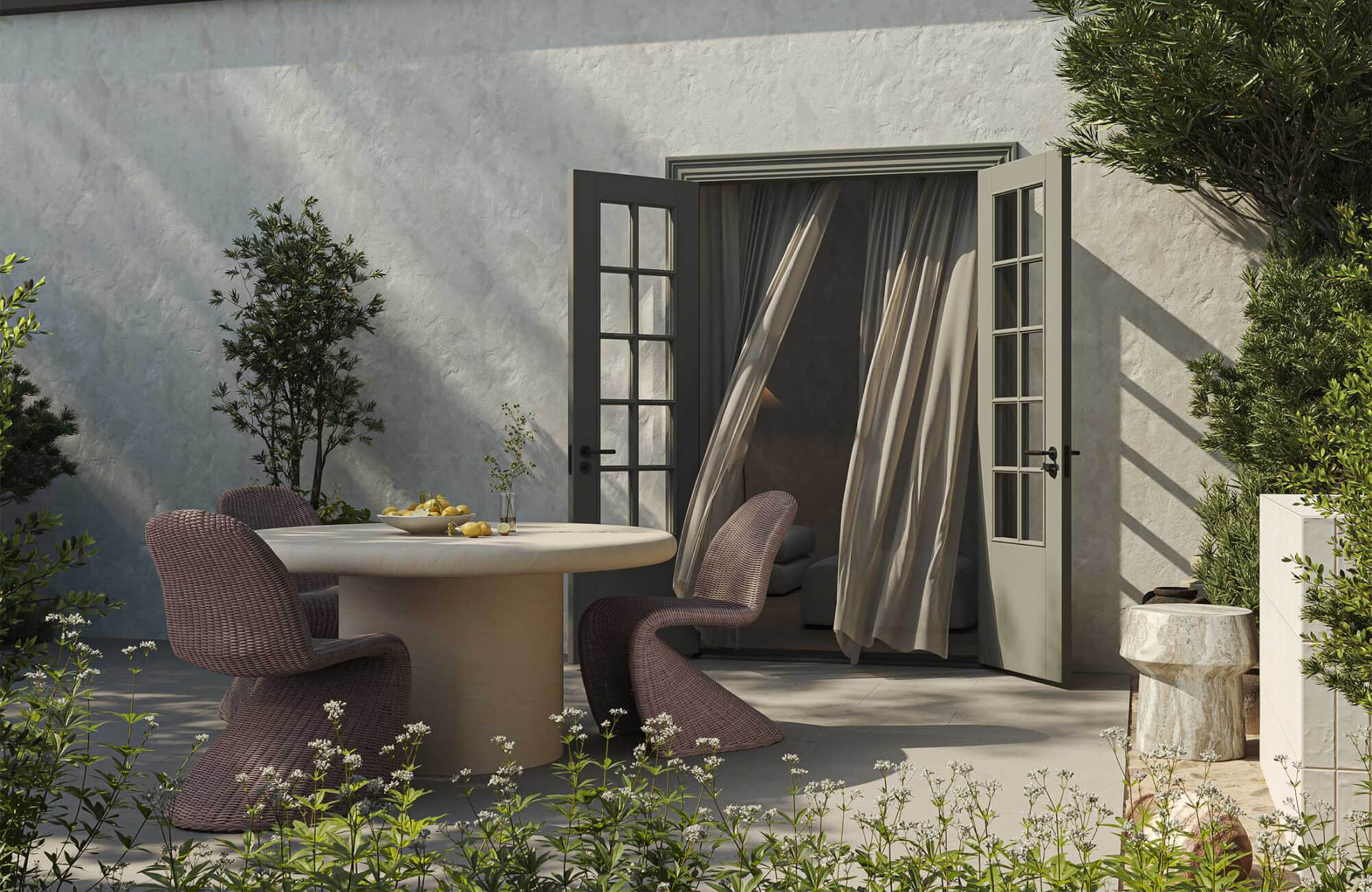 null A sculptural round dining table paired with curved woven chairs creates an intimate setting beside open French doors and layered garden plantings.