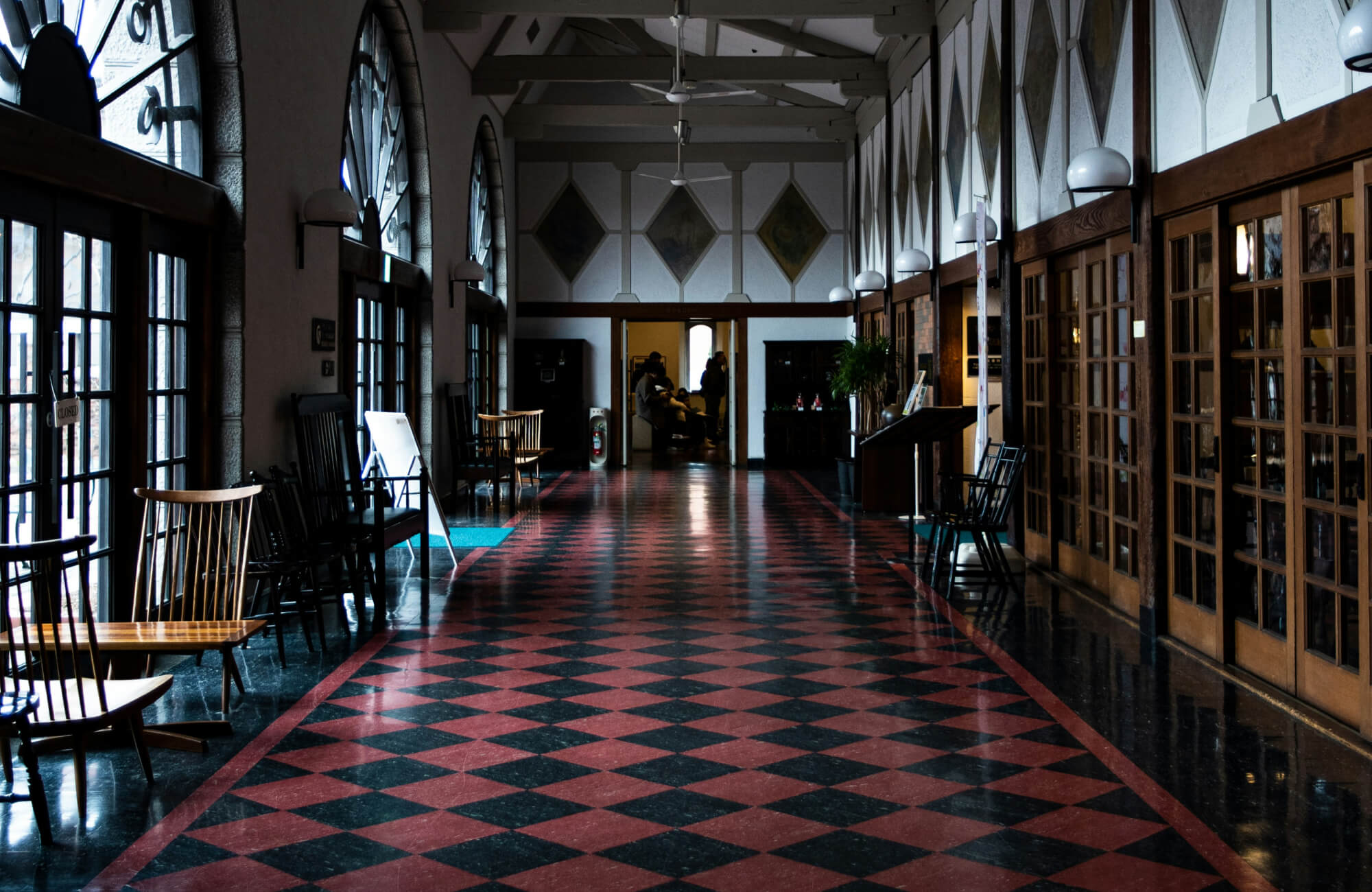 Classic hallway featuring red and black checkerboard tiles, large arched windows, and wooden accents, creating a timeless and inviting atmosphere