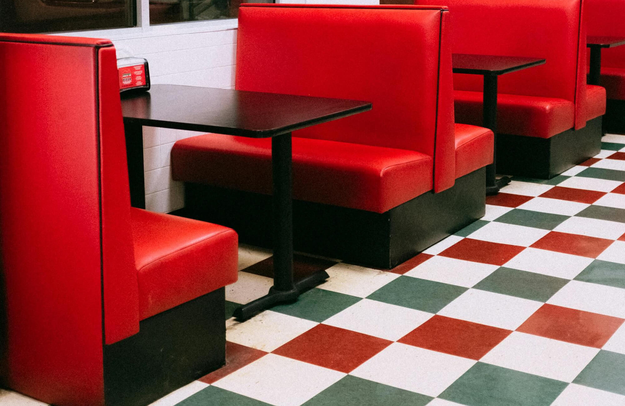 Retro diner scene with red vinyl booths and a bold red, green, and white checkerboard tile floor.