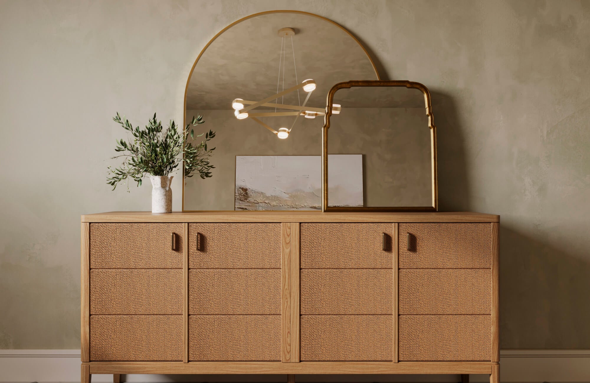 null A large arched mirror reflecting a modern chandelier, styled with a textured wood console, gold accent mirror, and greenery for a soft, organic interior feel.