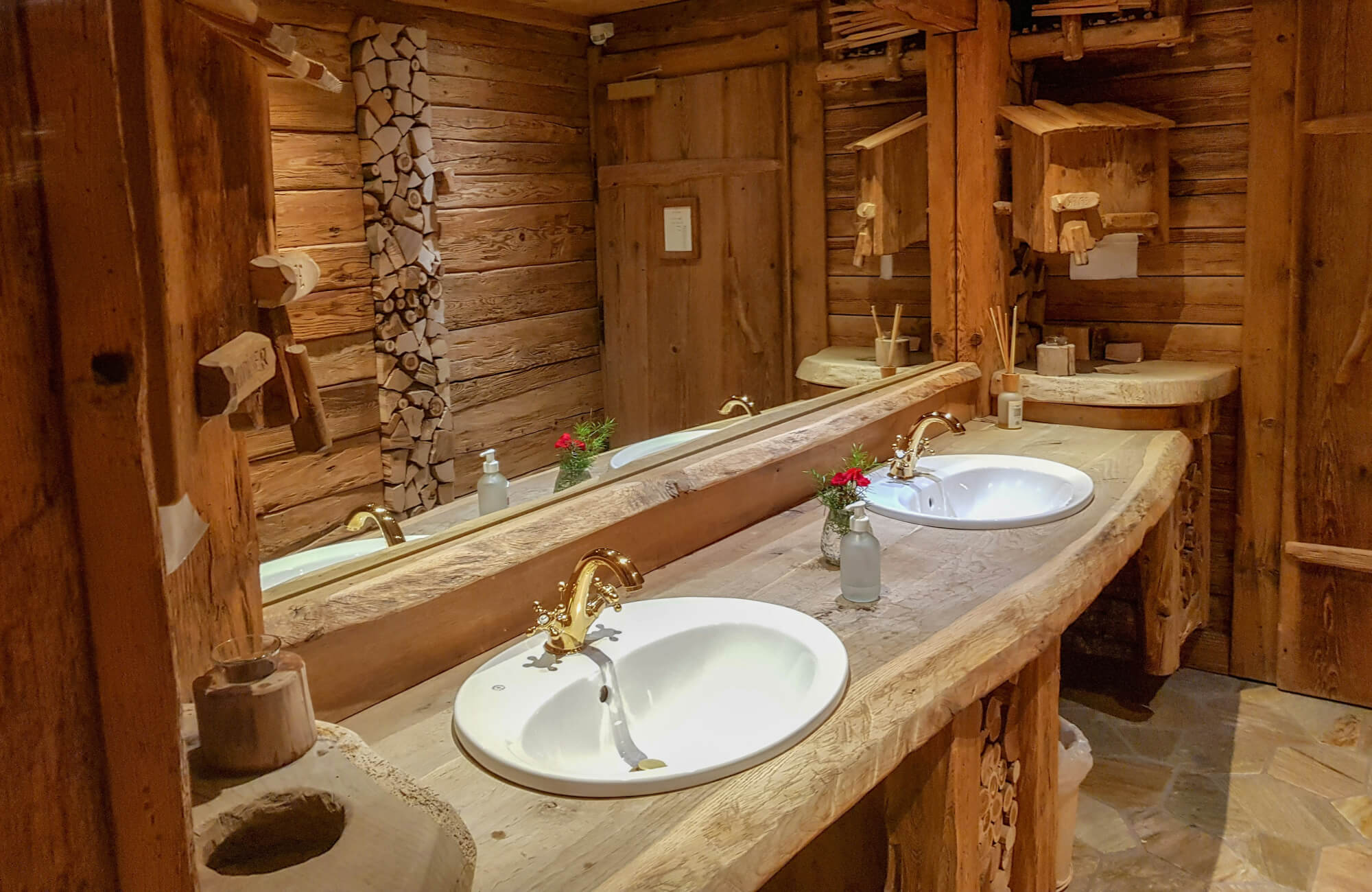 Cozy rustic bathroom with heavy wood textures, carved vanity details, and warm lighting throughout the space.
