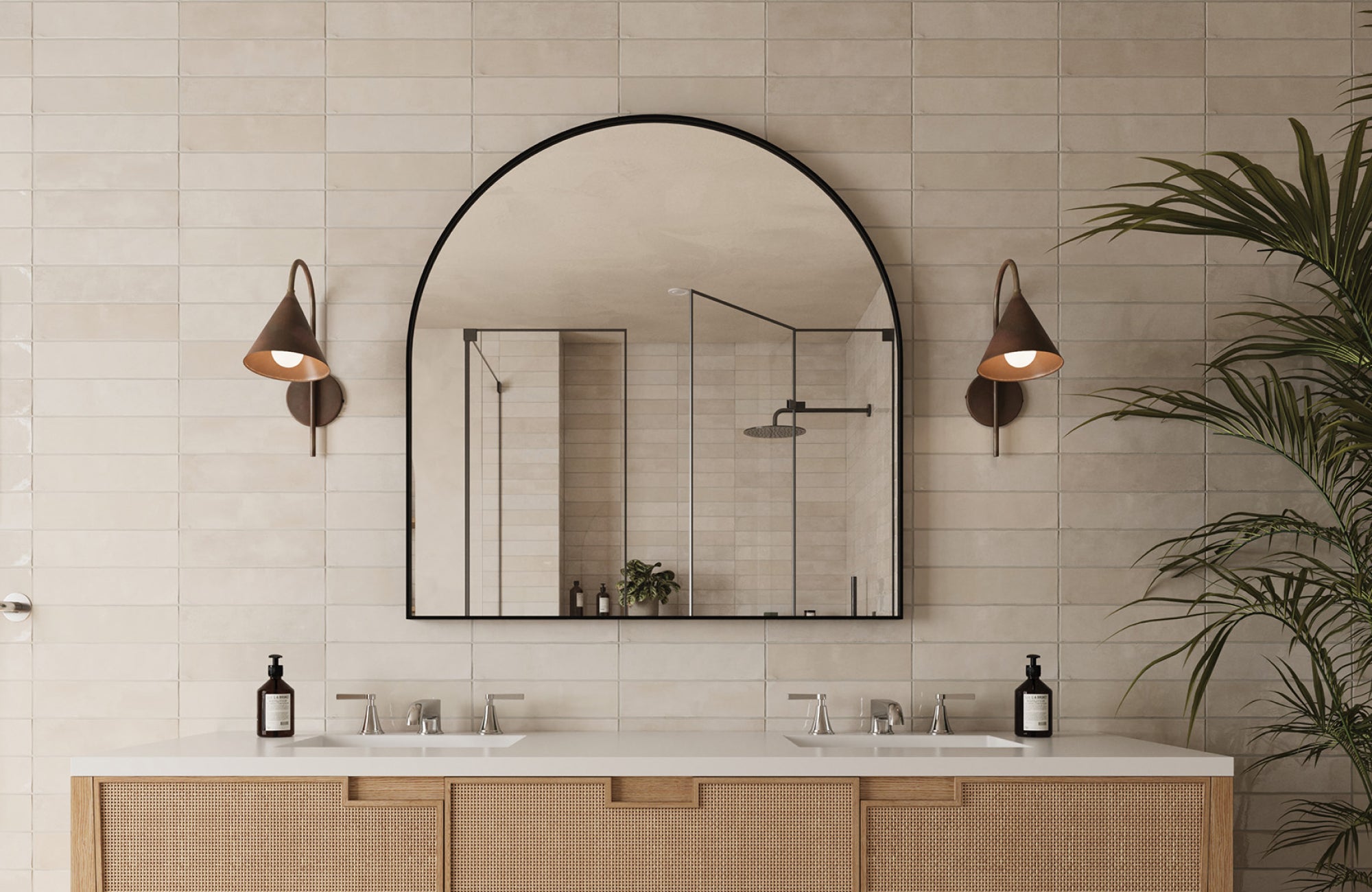 Arched black-framed mirror matching double sink width, flanked by sconces on beige tiled wall.