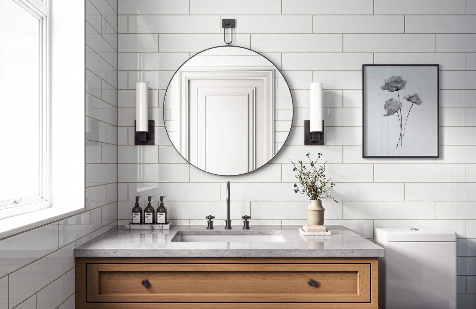 Round mirror centered over medium-width sink with side sconces and wood vanity in white-tiled bath.