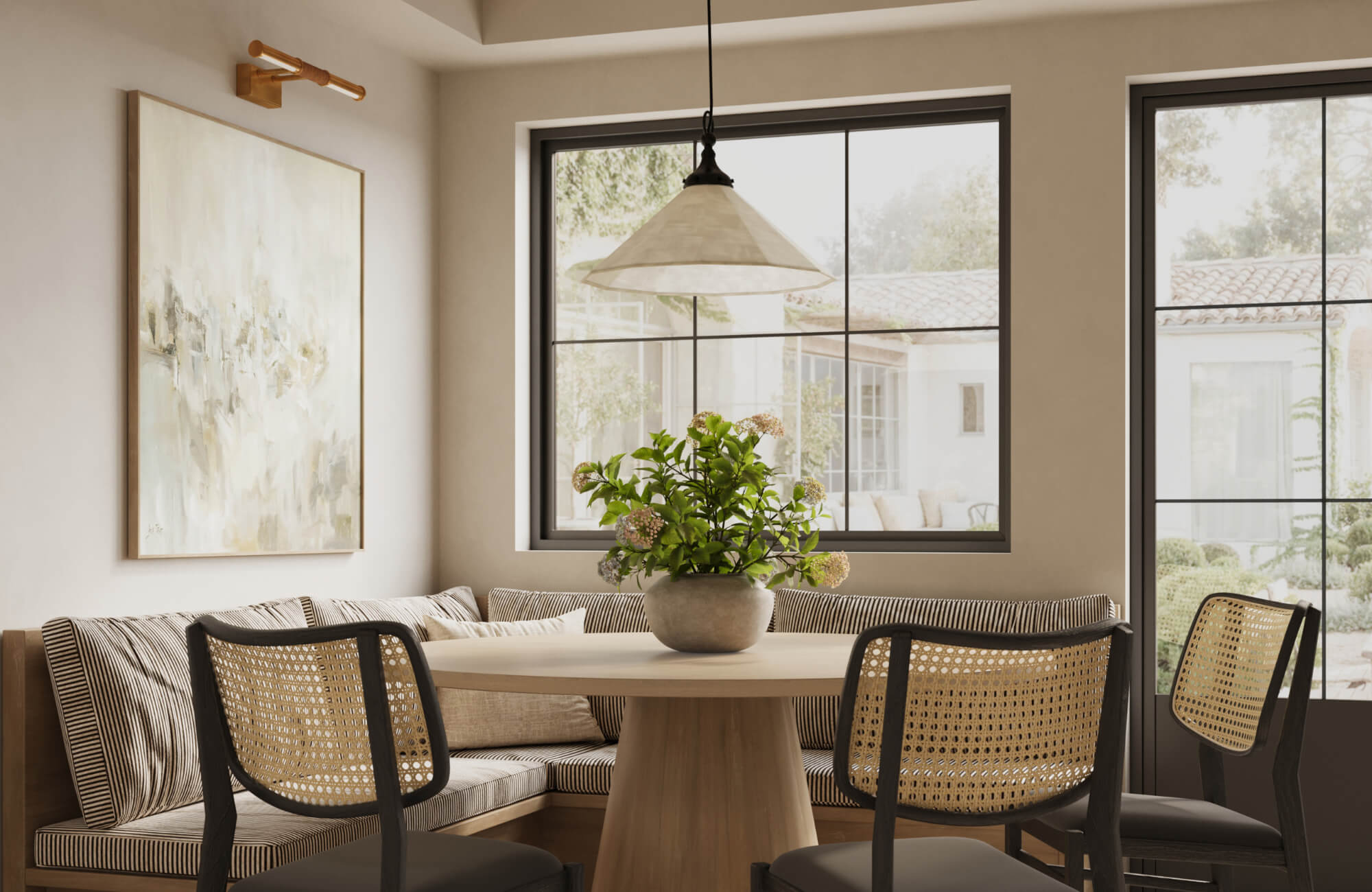 null A bright breakfast nook with a light wood table, woven chairs, and a large abstract painting illuminated by a brass picture light.