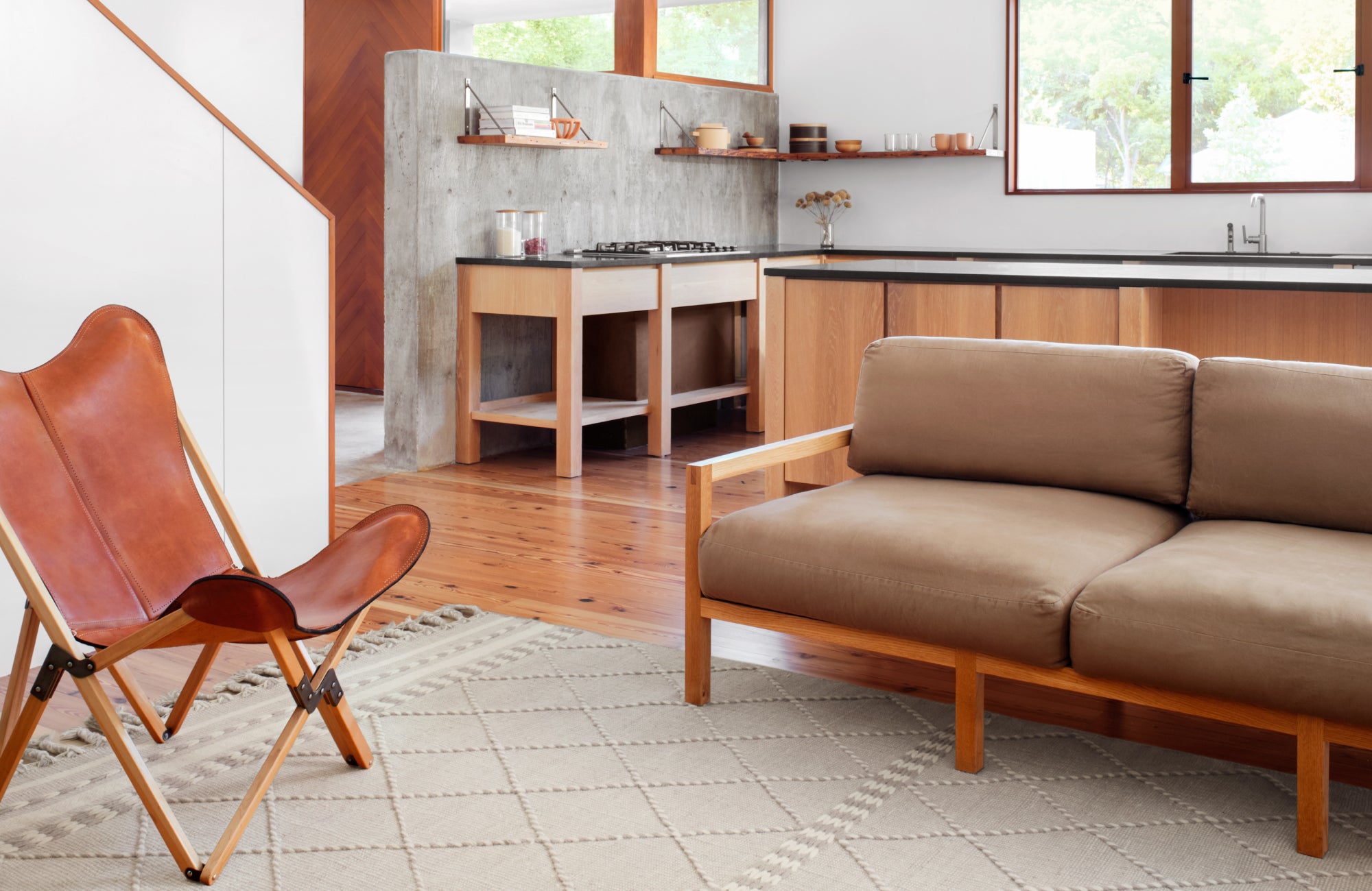 A modern open-plan kitchen and living area featuring the Lafferty Wool Blend Rug in Dove, a light-toned rug that softens the warm wood flooring.