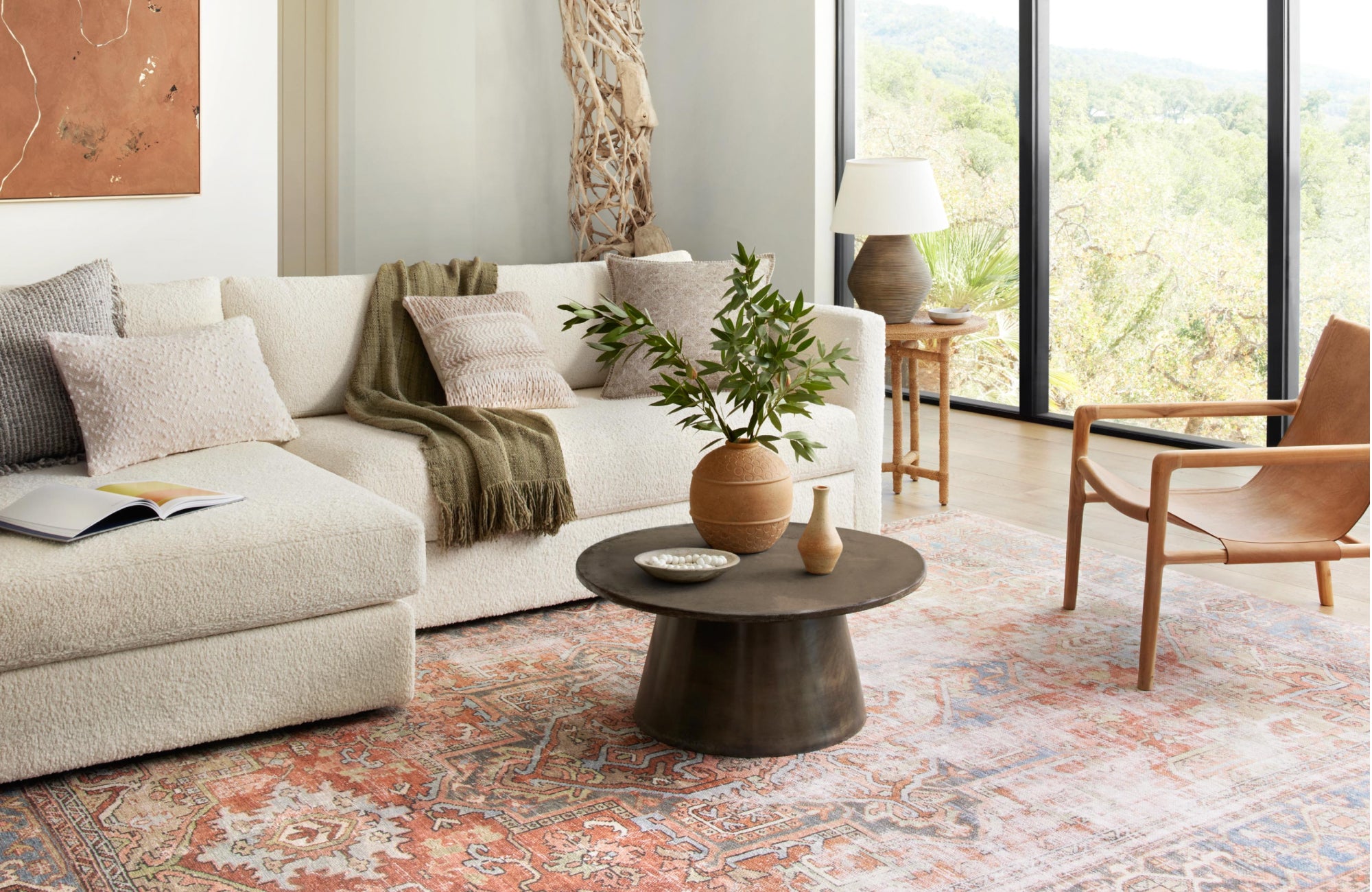 A sun-filled living room with a light cream sectional sofa, leather accent chair, and a coral-toned light rug that enhances the airy, coastal-inspired vibe.