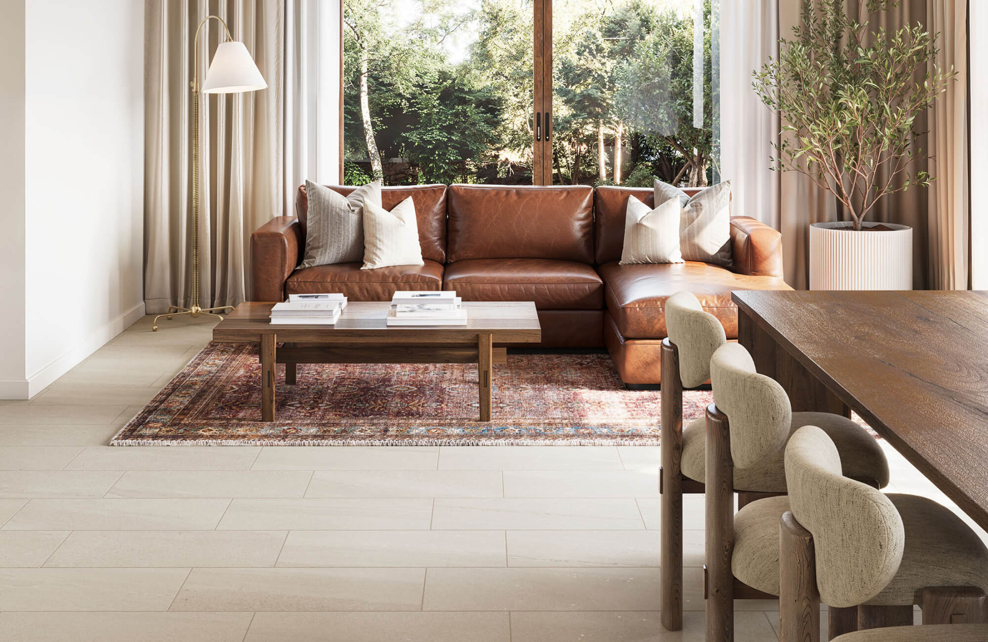 Open-layout living space featuring a rich brown leather sectional, vintage rug, and light beige large-format floor tiles.