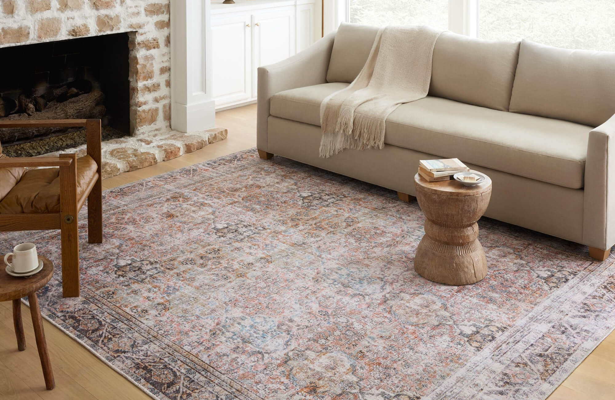 Inviting living room with a faded vintage-style rug, neutral sofa, rustic stone fireplace, and light wood flooring.