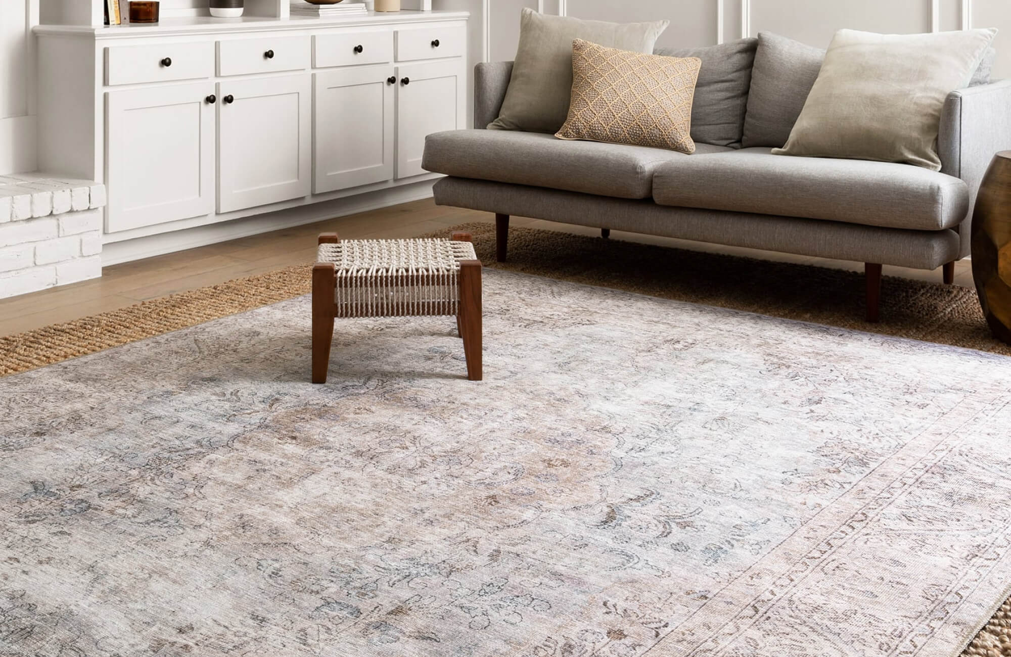 Neutral-toned living room with a faded vintage rug, mid-century grey sofa, and layered textures for a relaxed, elegant look.
