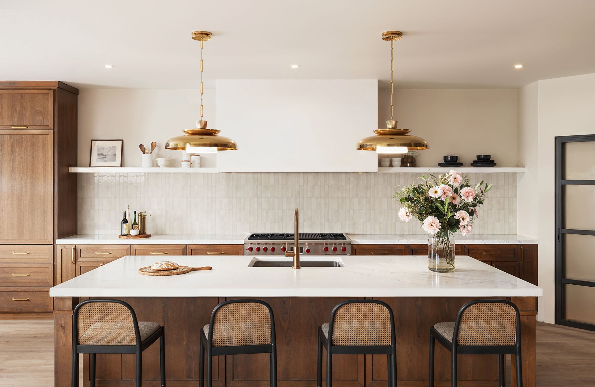 Pendant lights and faucet in polished brass finish add warmth and shine to a kitchen with wood cabinetry and white counters.