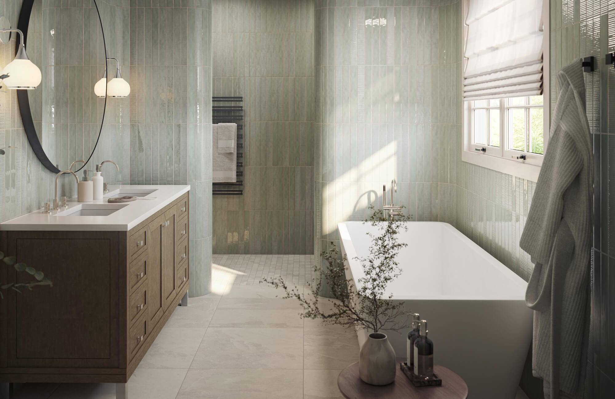 Modern bathroom with glossy green vertical subway tile walls, freestanding tub, wood vanity, round mirror, sconces, and gray stone look tile flooring.
